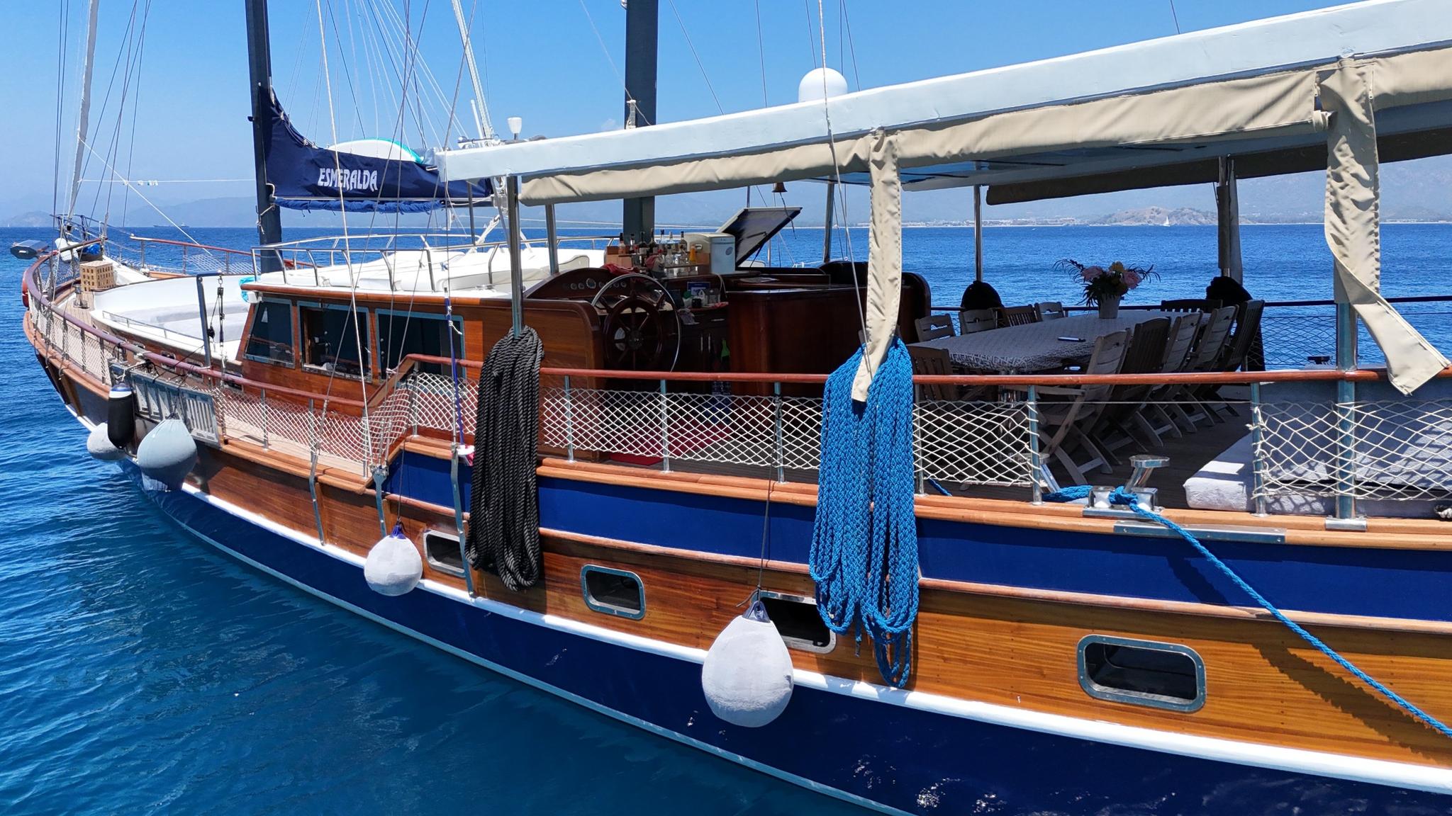 Traditional wooden gulet with blue hull, varnished deck, white canvas awning and helm area