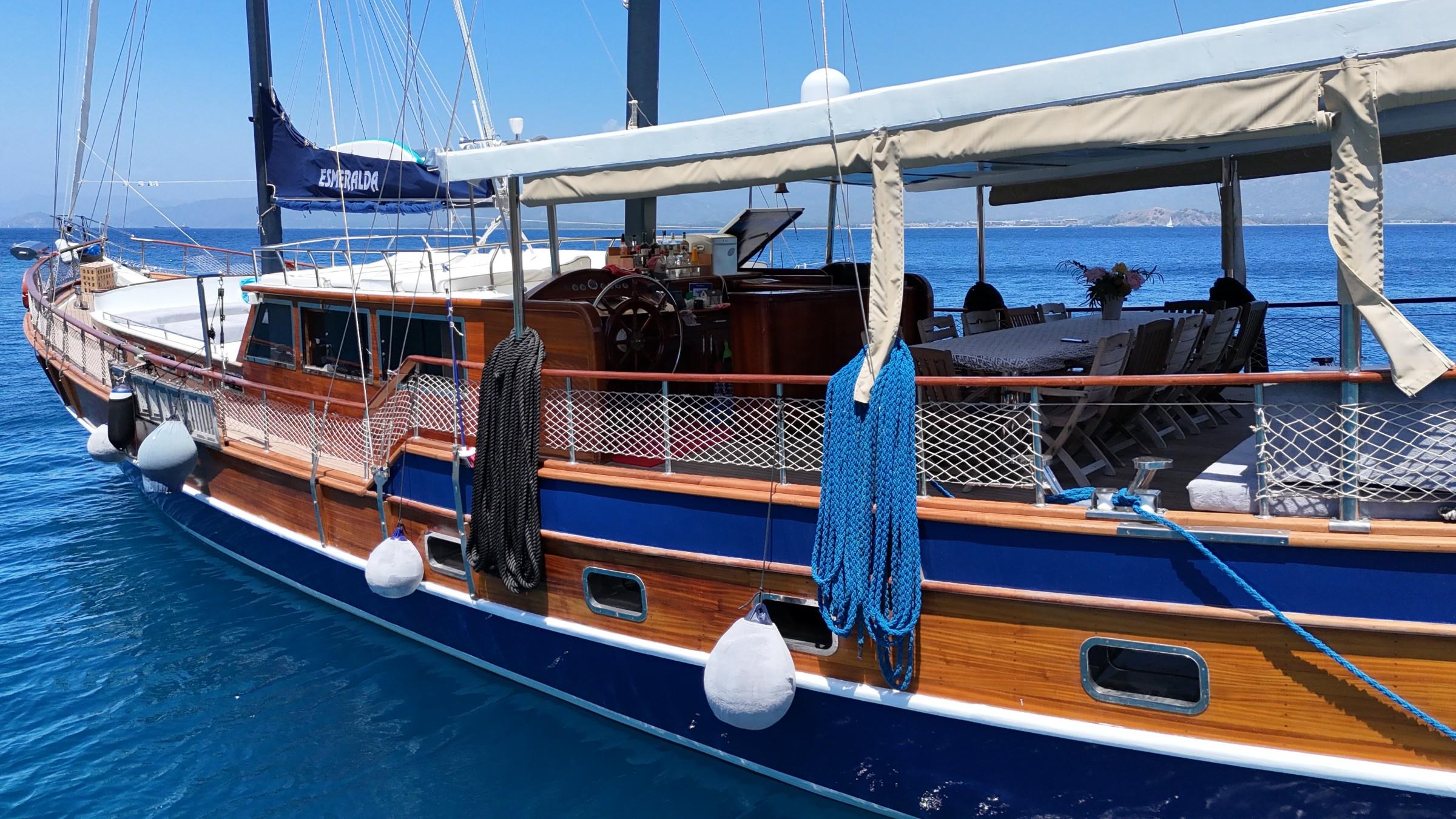 Traditional wooden gulet with blue hull, varnished deck, white canvas awning and helm area