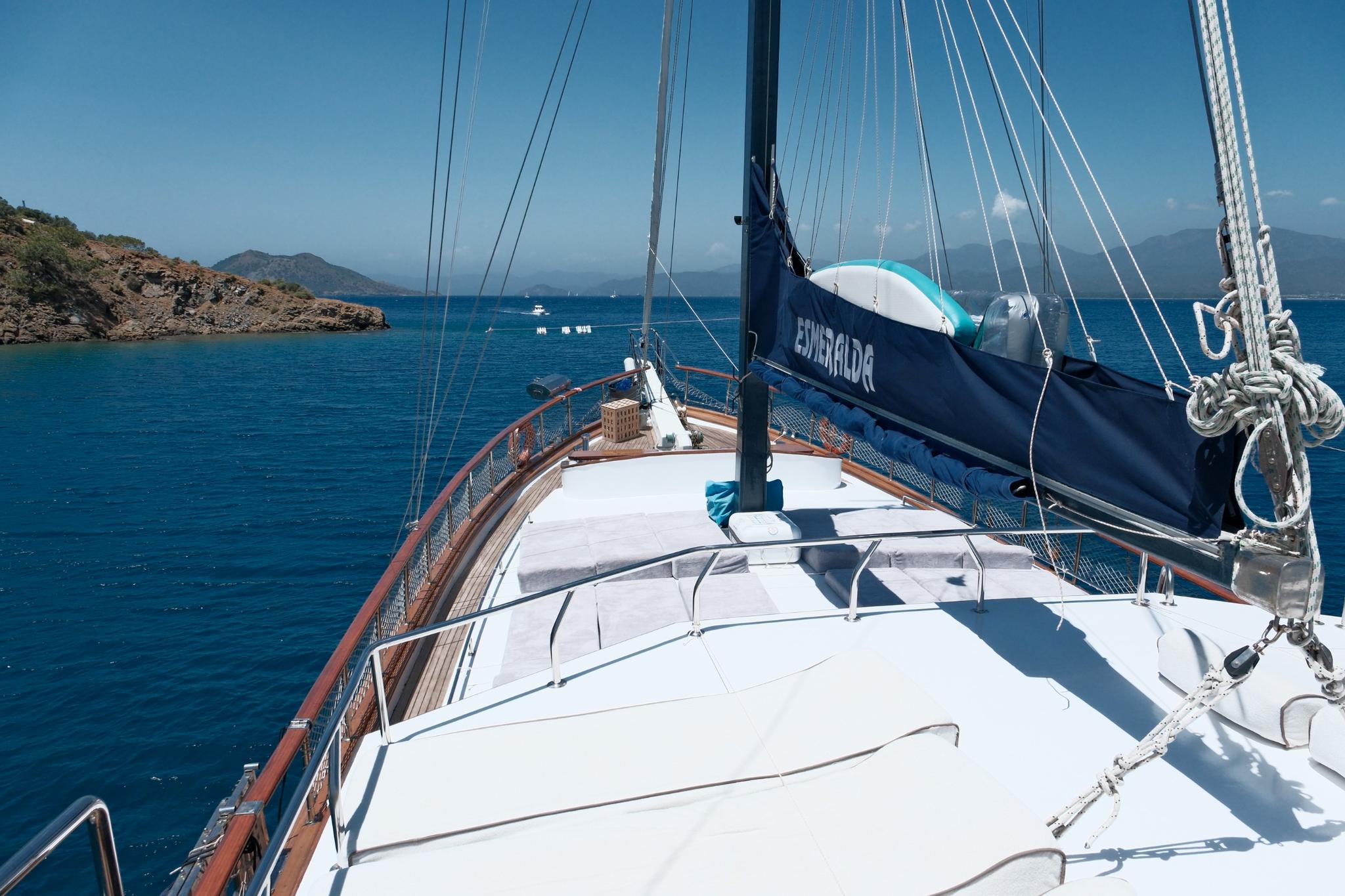 Gulet bow deck with wooden planking, mast, rigging and blue sail unfurled at sea