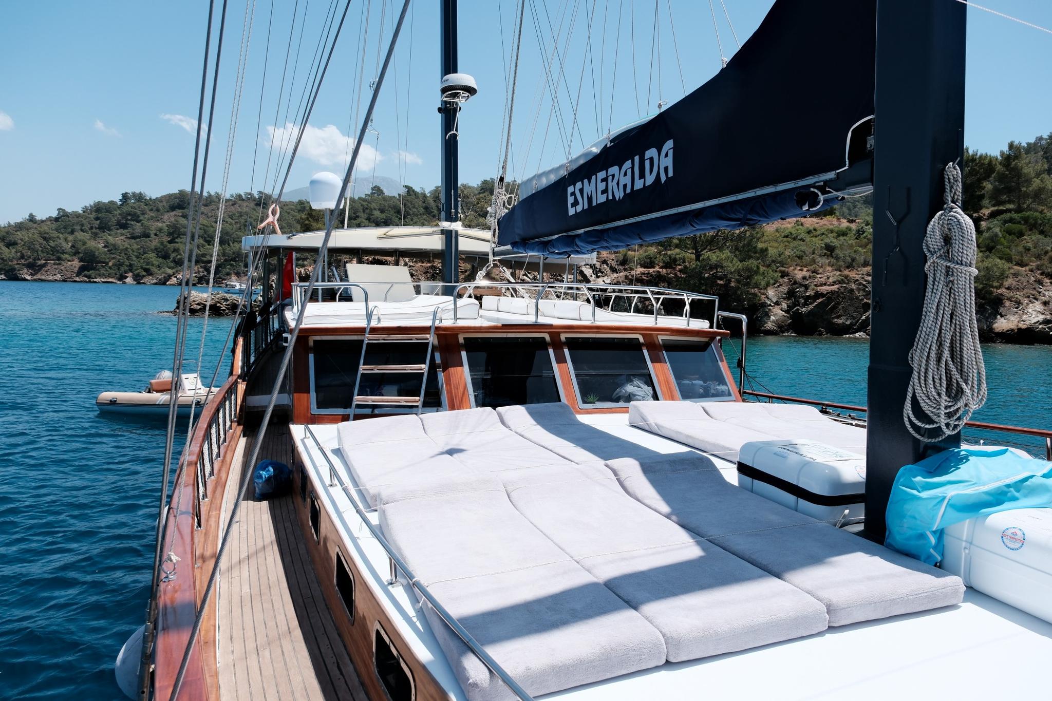 Gulet forward deck with white cushioned seating area and dark blue sail