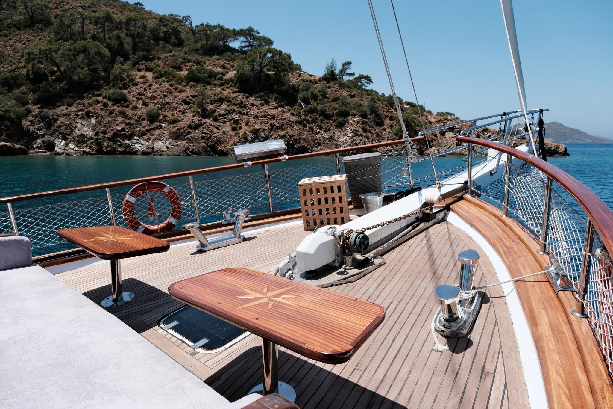 Forward deck of sailing yacht with teak dining table, safety netting, and windlass equipment