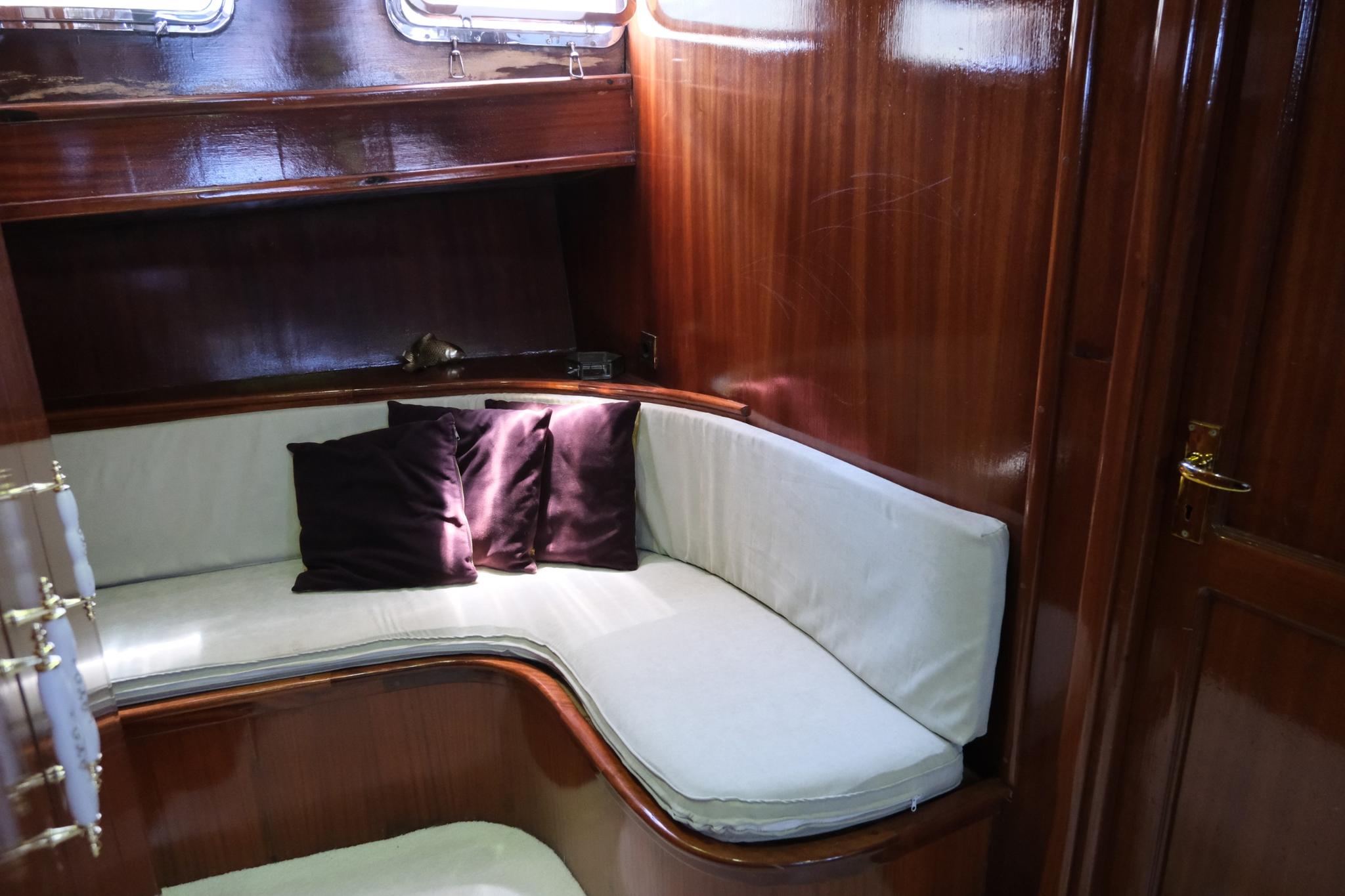 yacht cabin interior featuring curved white upholstered seating with purple accent pillows