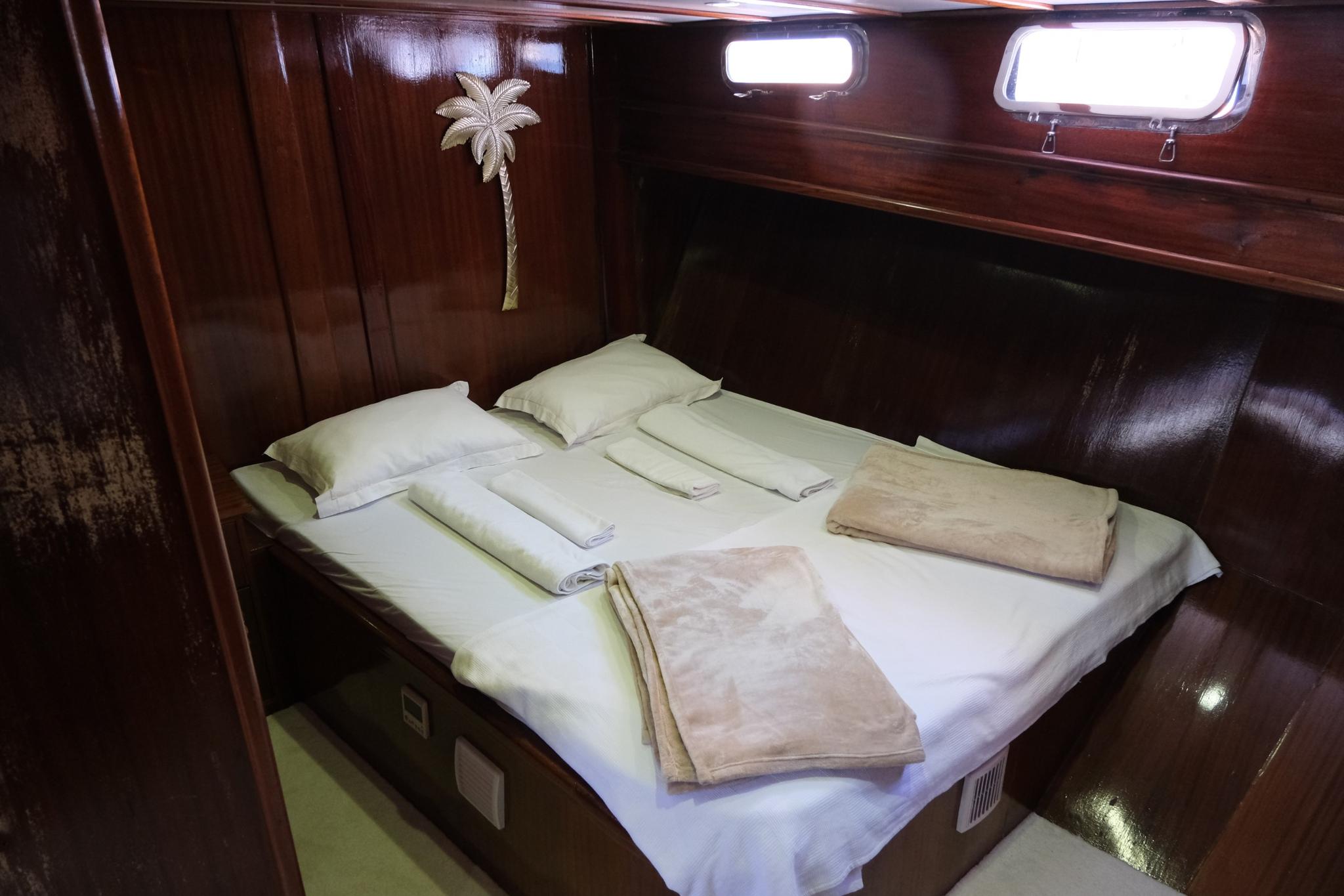 yacht guest cabin with double bed, white linens, wooden paneling and portholes