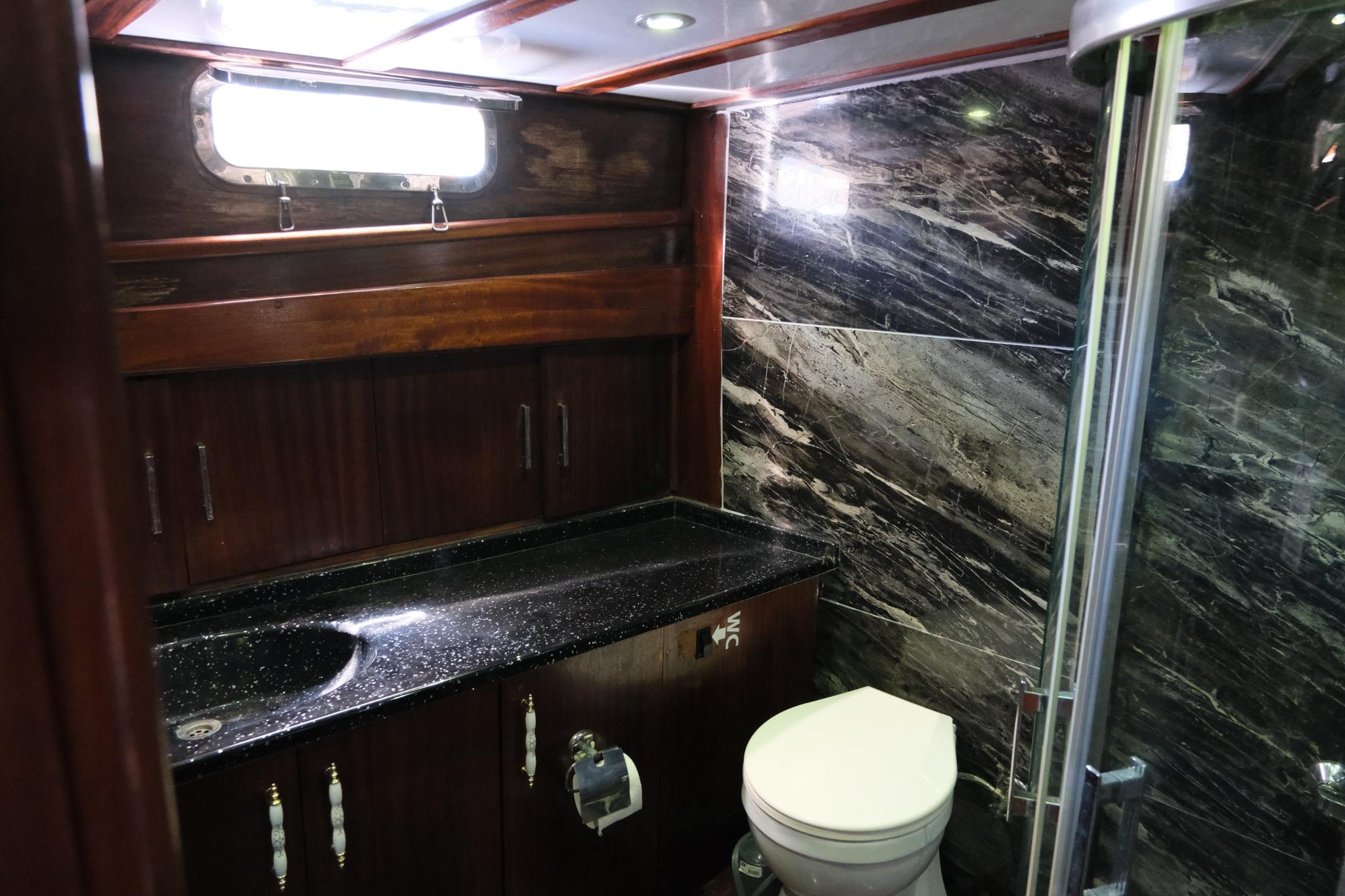 luxury yacht bathroom featuring dark marble walls, black granite vanity, white toilet and glass shower