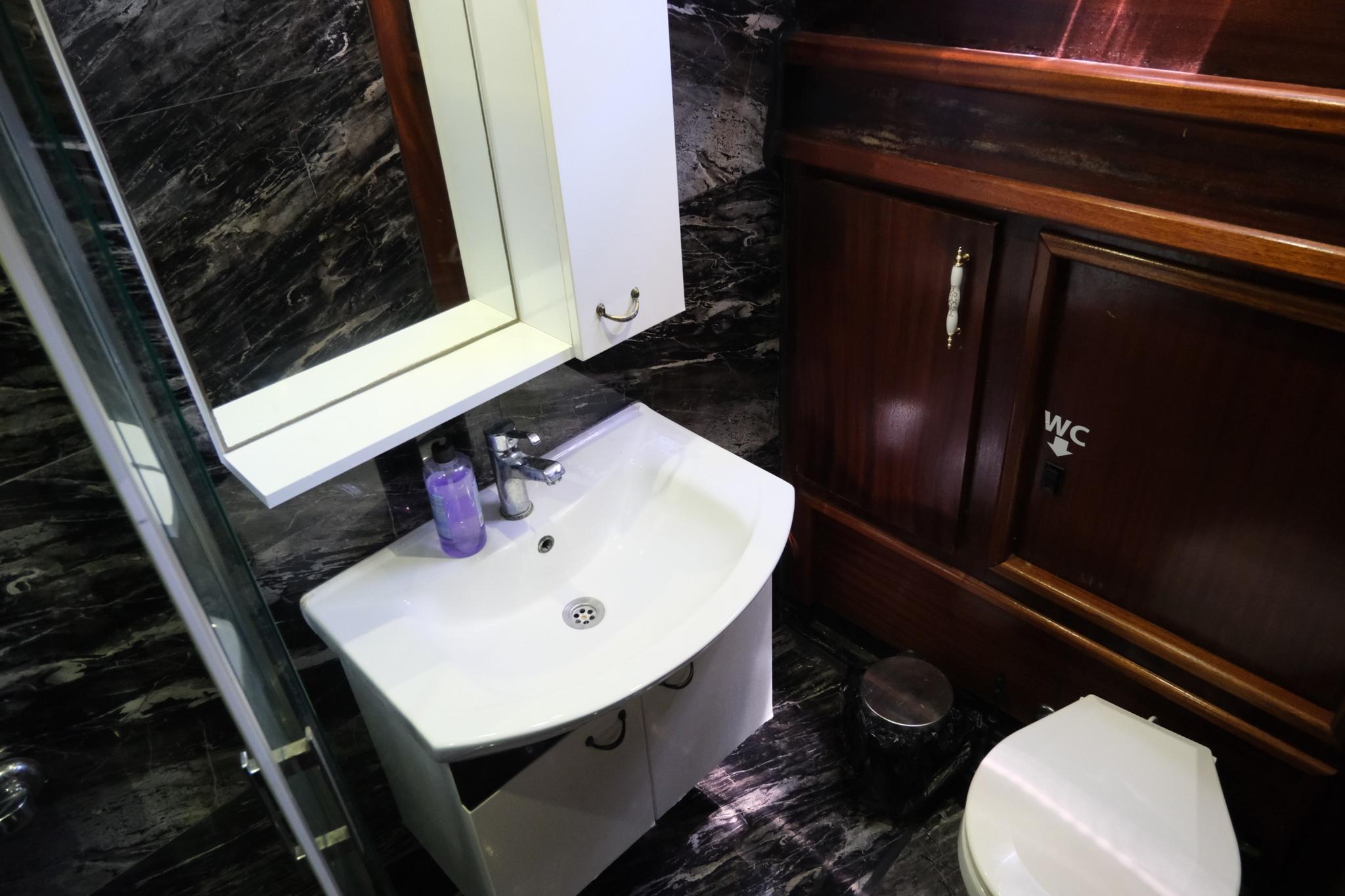 compact yacht bathroom featuring white basin, mirror, dark marble walls and wooden storage cabinet
