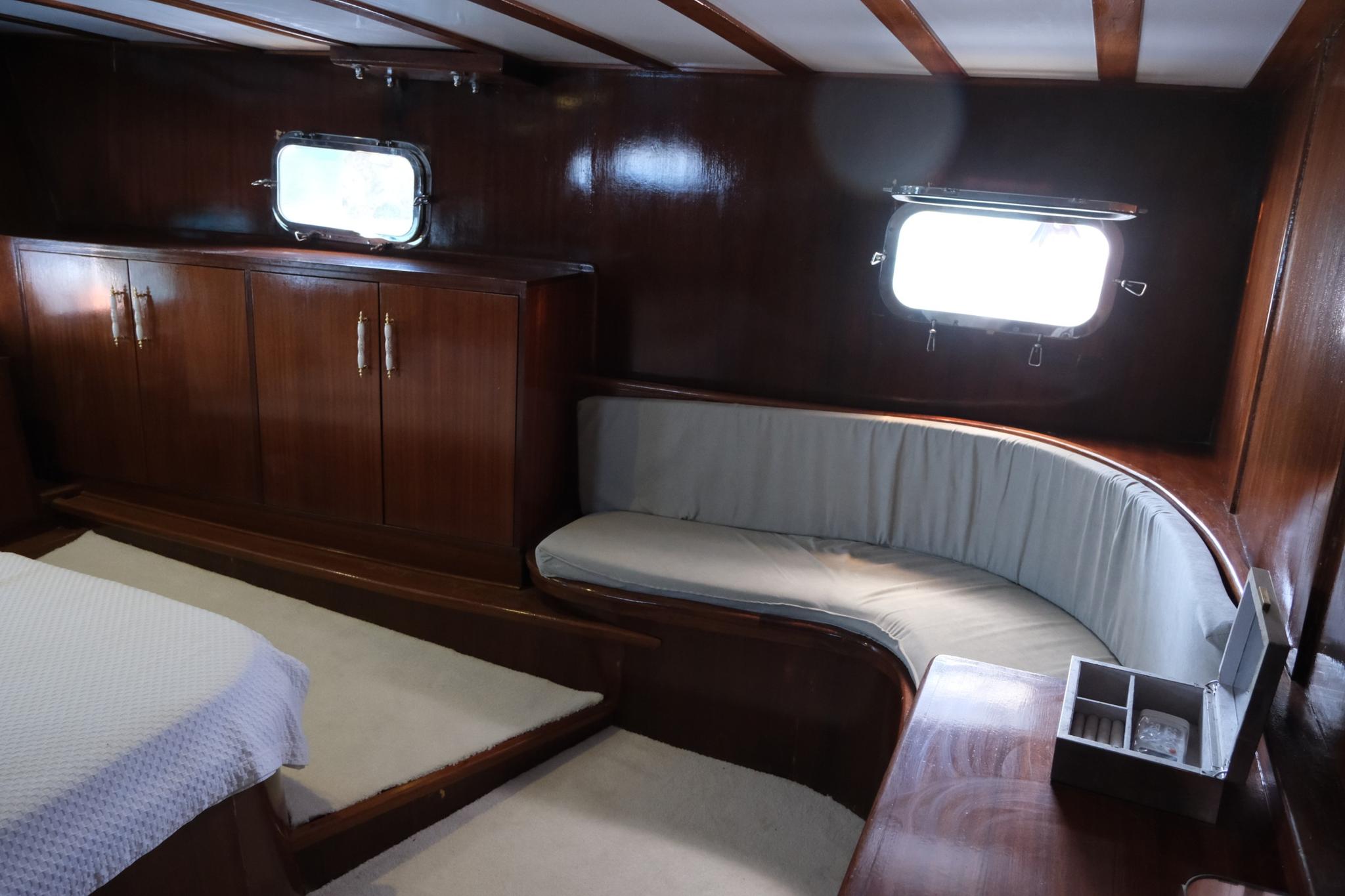 yacht cabin interior featuring bed, curved bench seating, wooden cabinetry and portholes