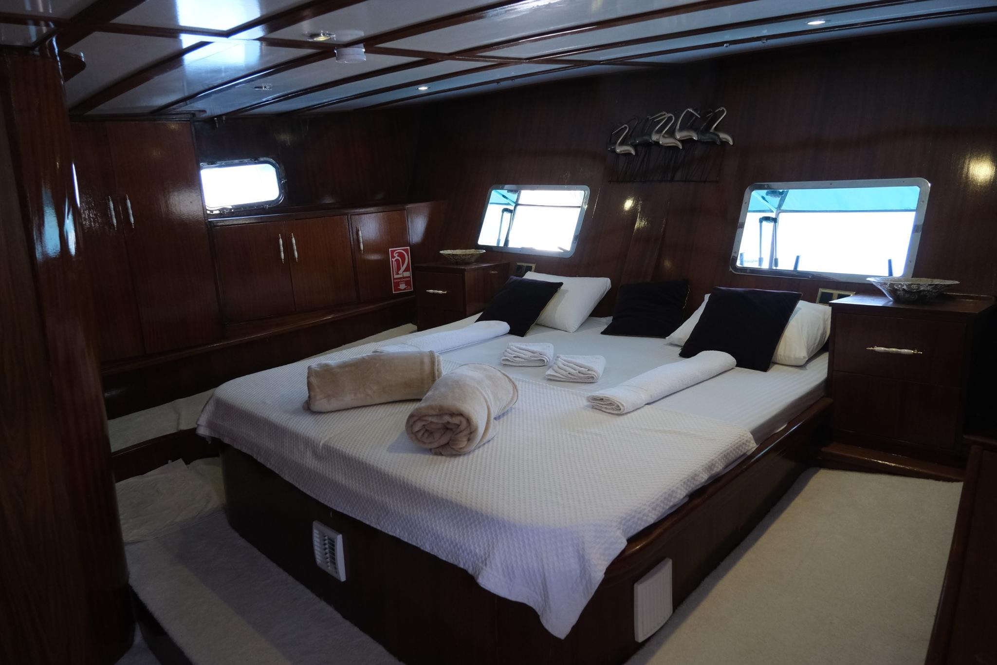 yacht cabin interior with white bedding, dark wood paneling, and three rectangular portholes