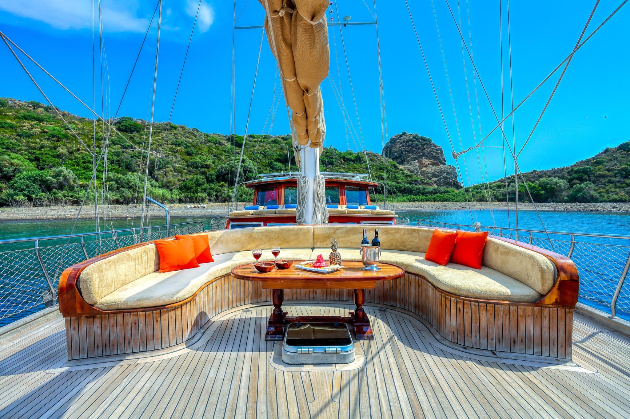 forward deck curved banquette seating with teak table and orange cushions on gulet
