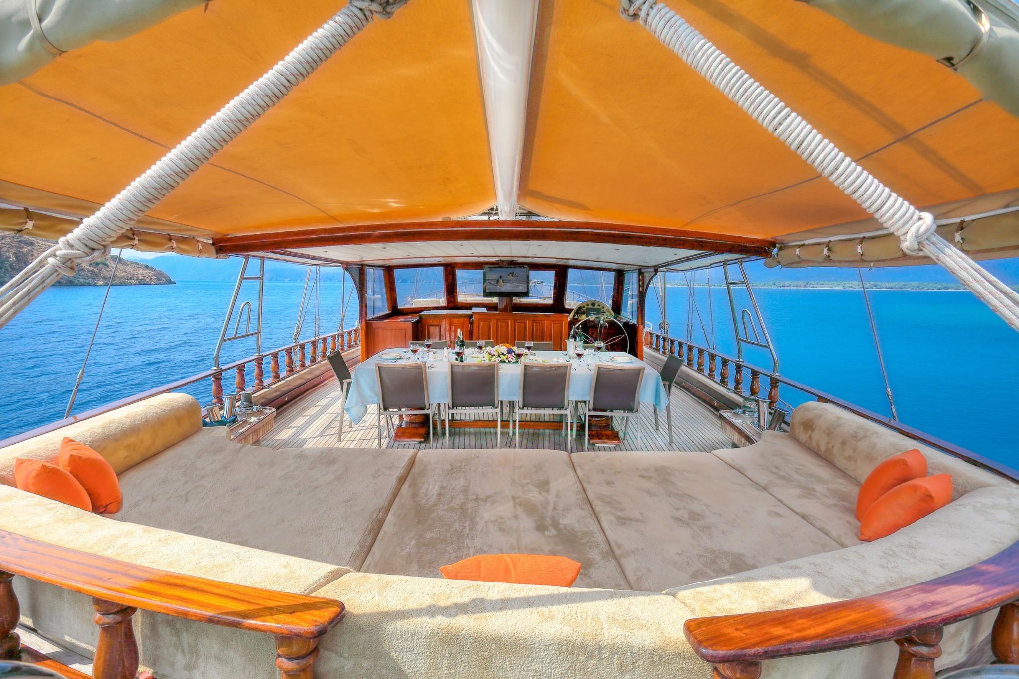 Gulet aft deck dining table with white chairs under orange canvas awning