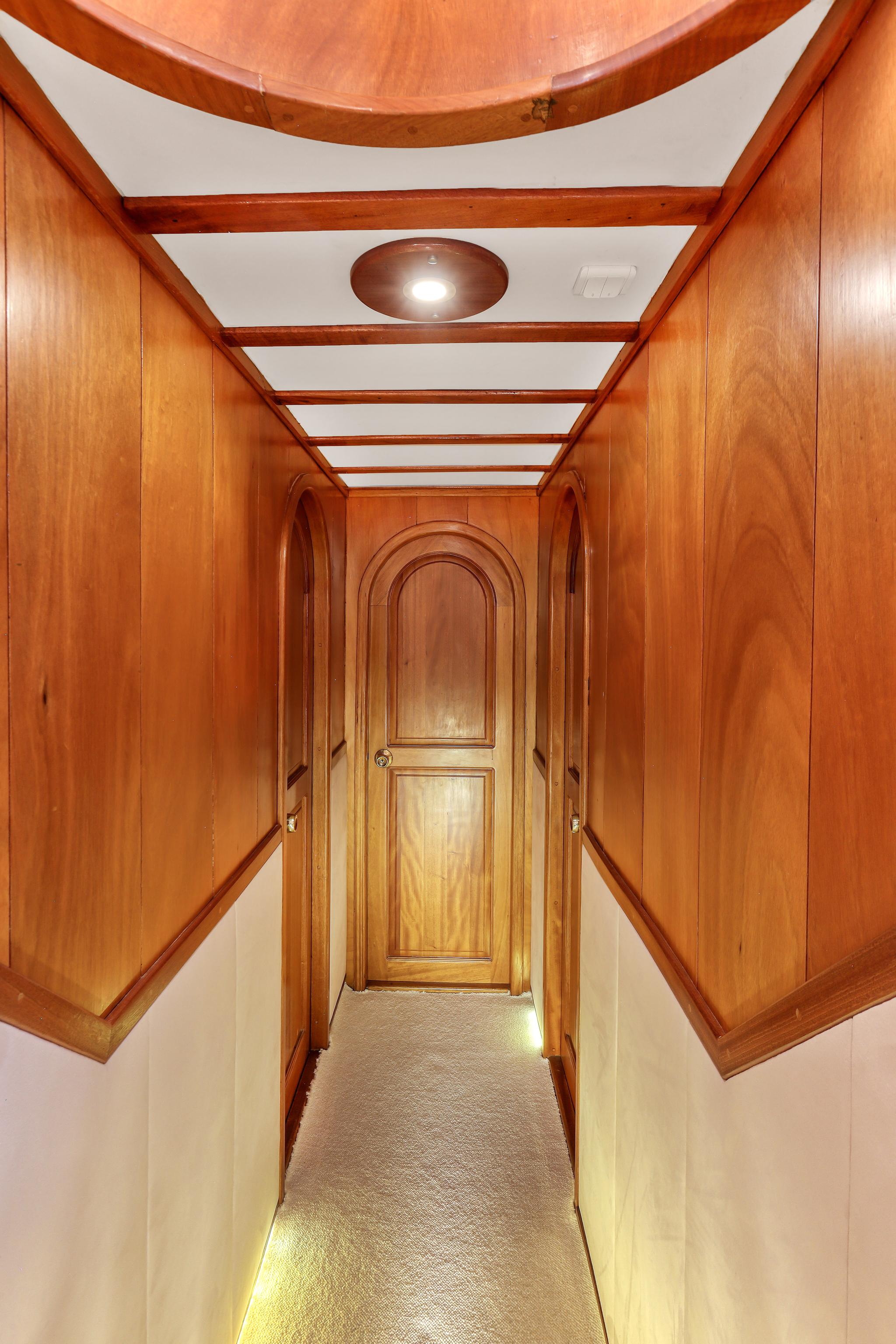yacht interior corridor with wood paneling leading to arched cabin door