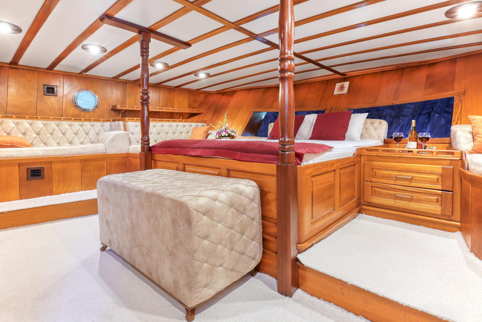 luxury yacht master cabin featuring four-poster bed with red bedding, quilted ottoman, and built-in seating