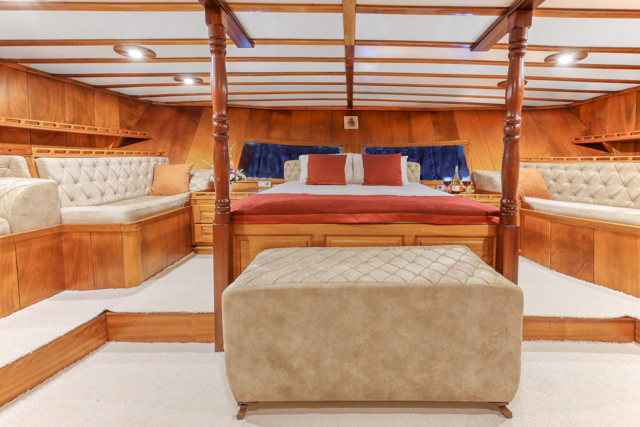 Master cabin featuring four-poster bed with red bedding, cream quilted seating areas and rich wood paneling