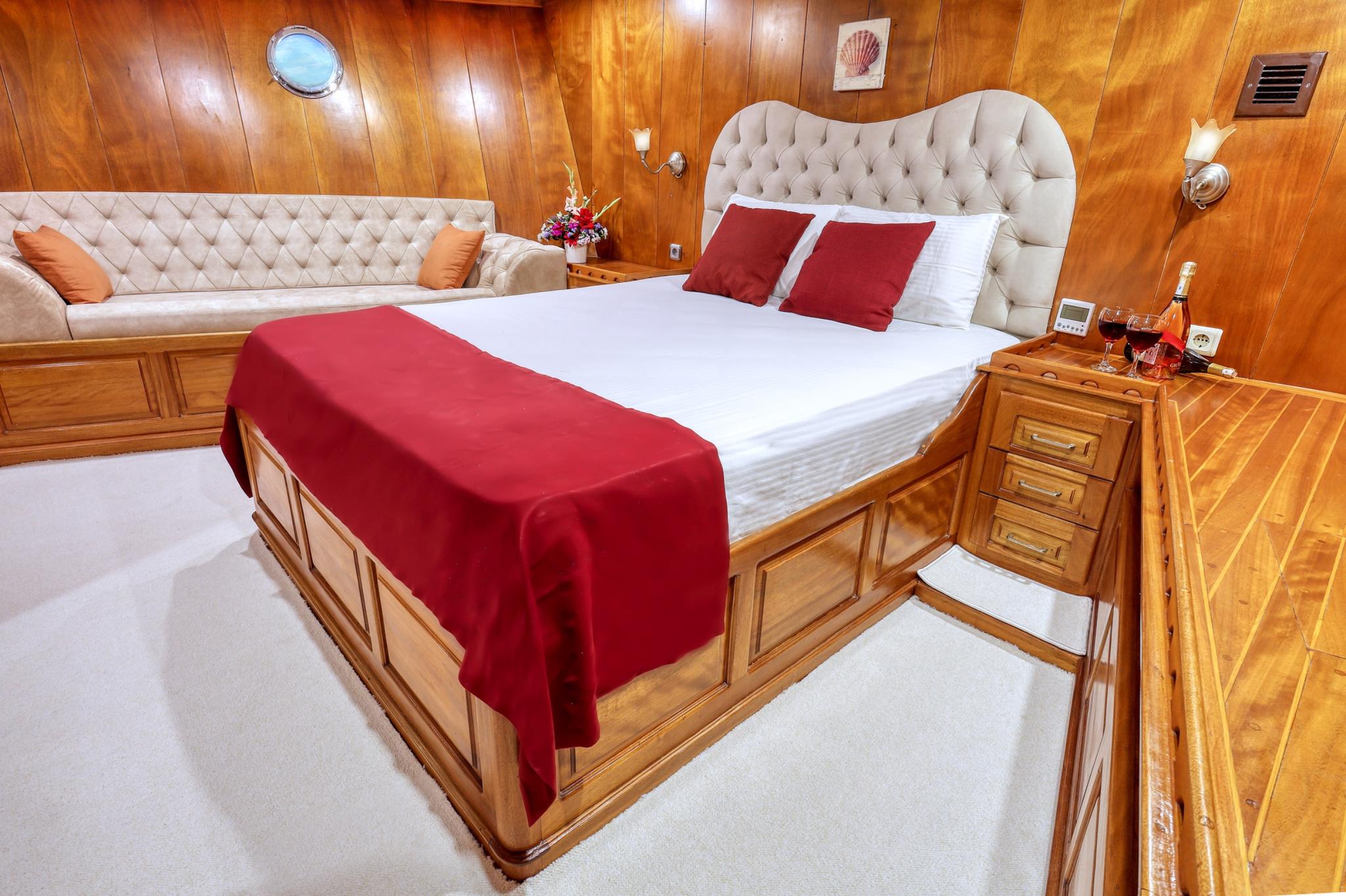 luxurious master cabin featuring king bed with red runner, cream tufted headboard, built-in seating