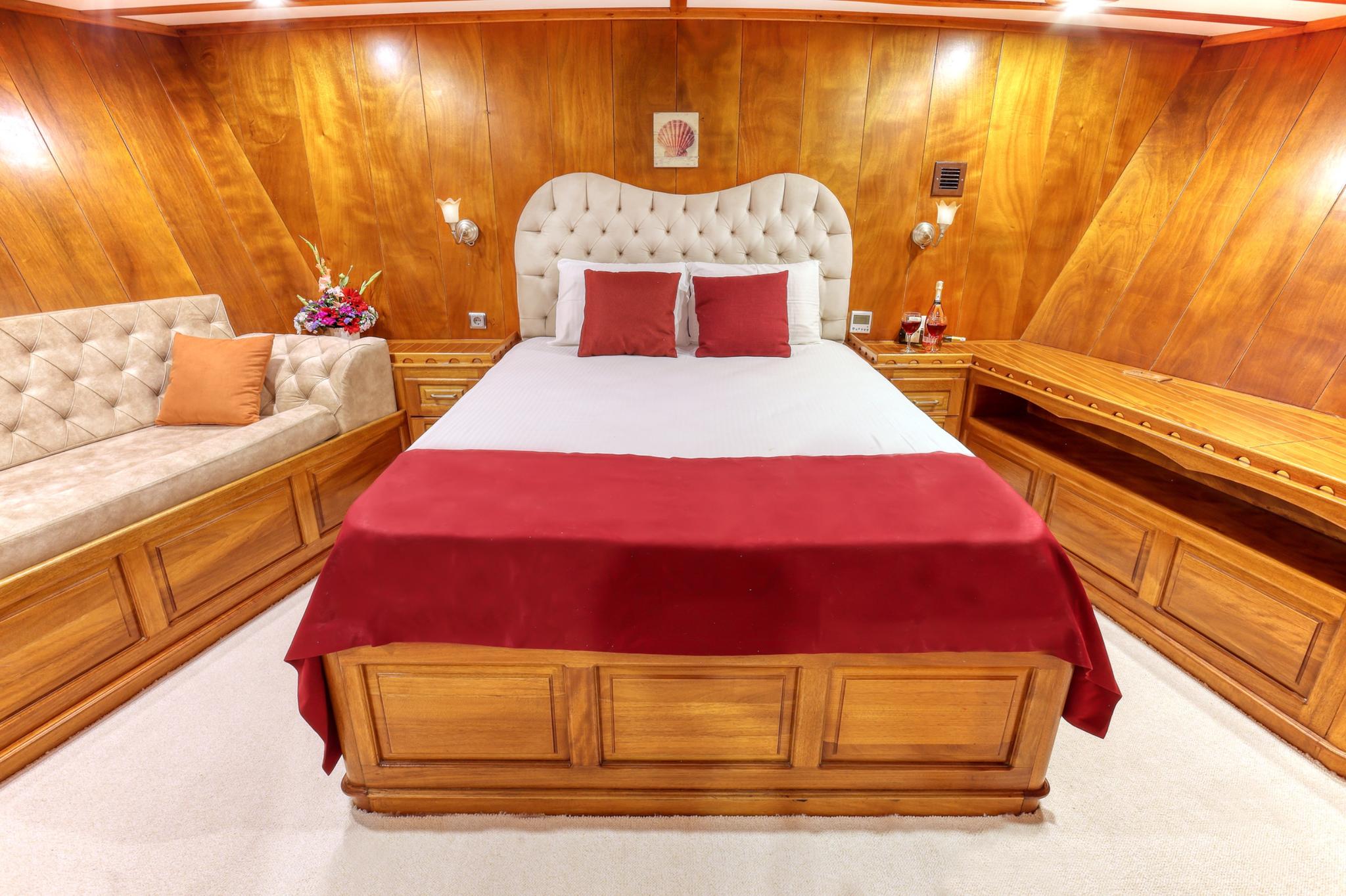 yacht master cabin with tufted headboard, red bedding, wood paneling and built-in seating