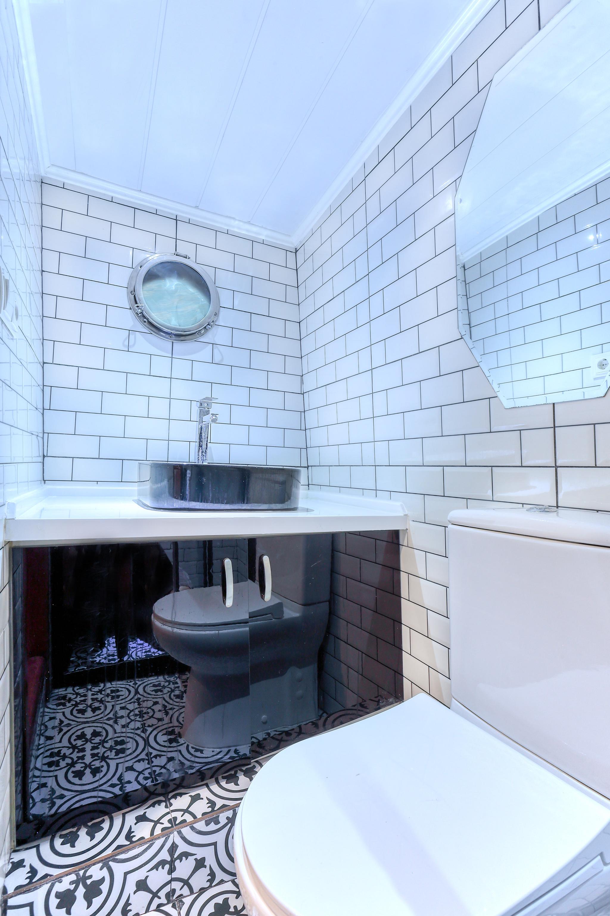 yacht bathroom featuring white subway tile walls, round porthole window, vessel sink and patterned floor tiles