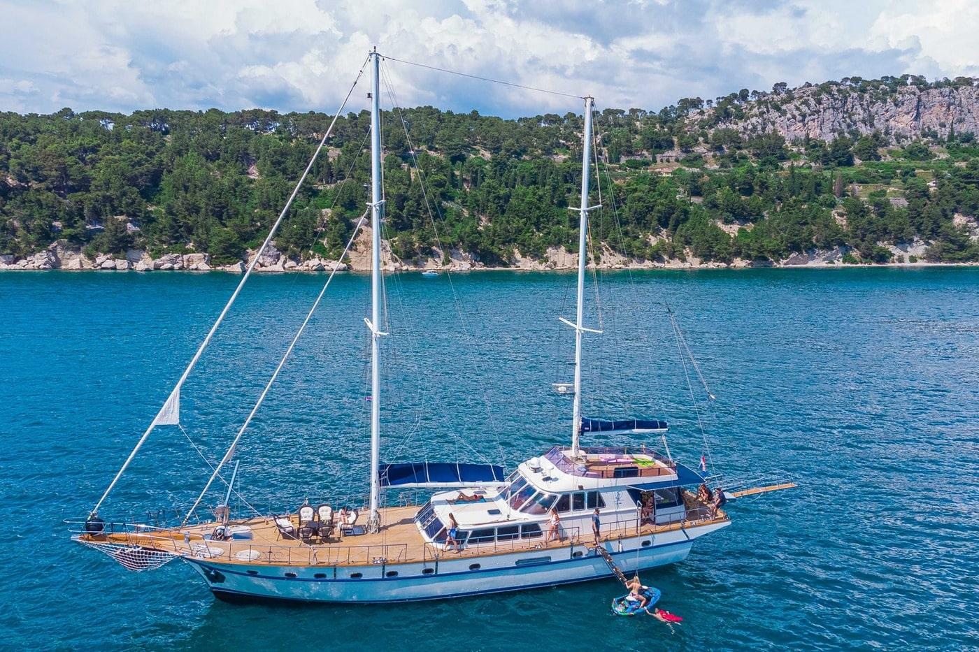 white gulet yacht anchored in turquoise bay with guests on deck and swimmer in water
