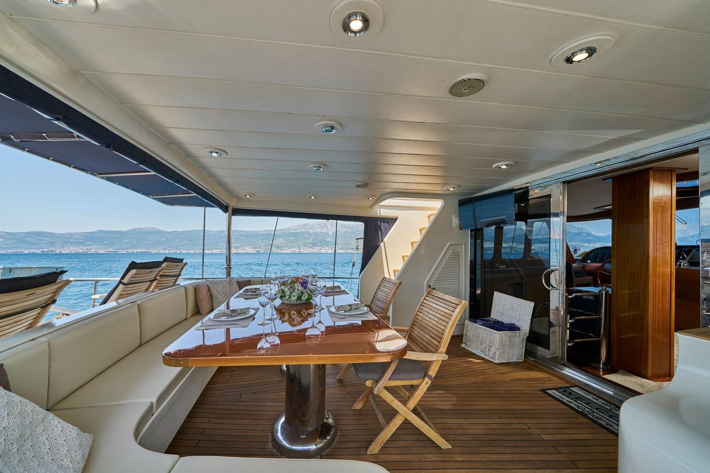 yacht aft deck dining area with wooden table, teak flooring, cream seating and coastal views