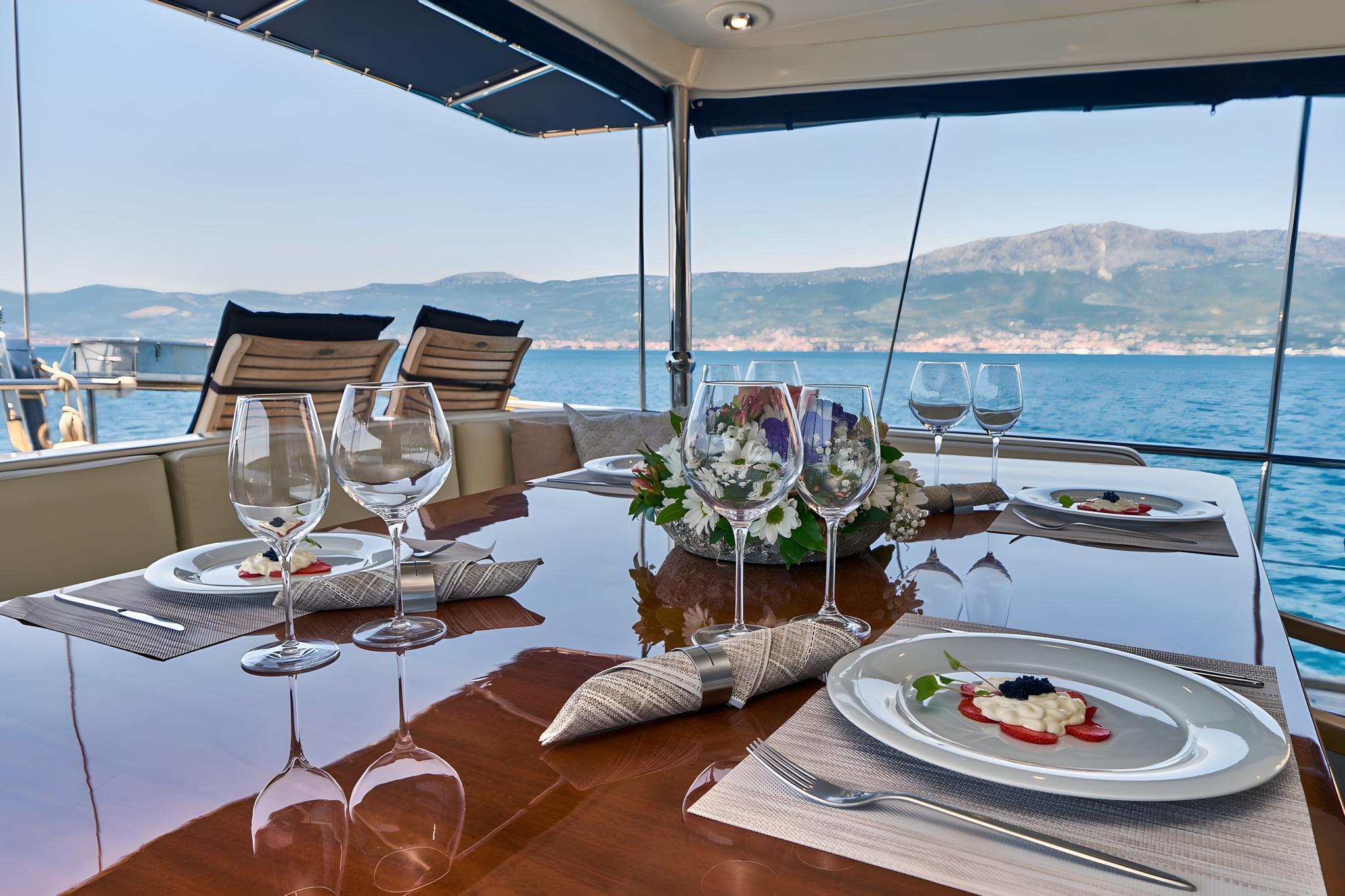 yacht dining table with plated gourmet food, wine glasses and floral centerpiece overlooking coastline