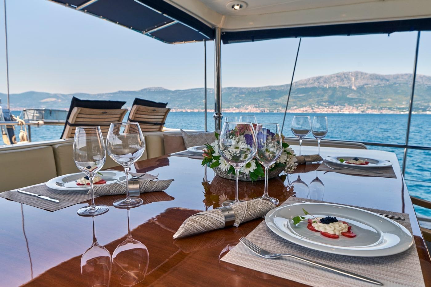 yacht dining table with plated gourmet food, wine glasses and floral centerpiece overlooking coastline