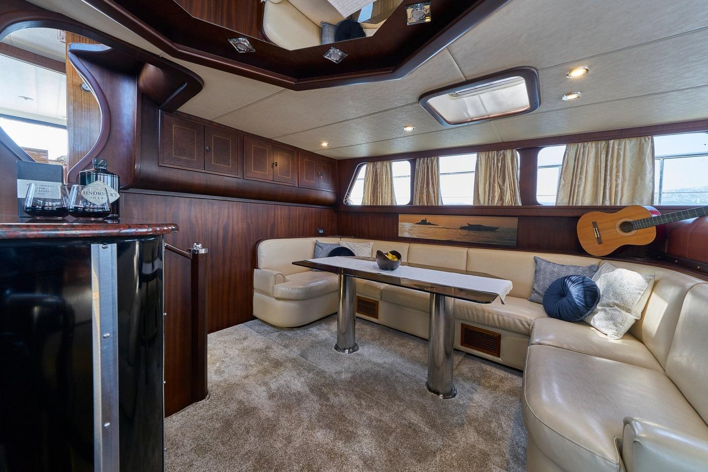 yacht interior salon with curved cream leather seating, coffee table and acoustic guitar