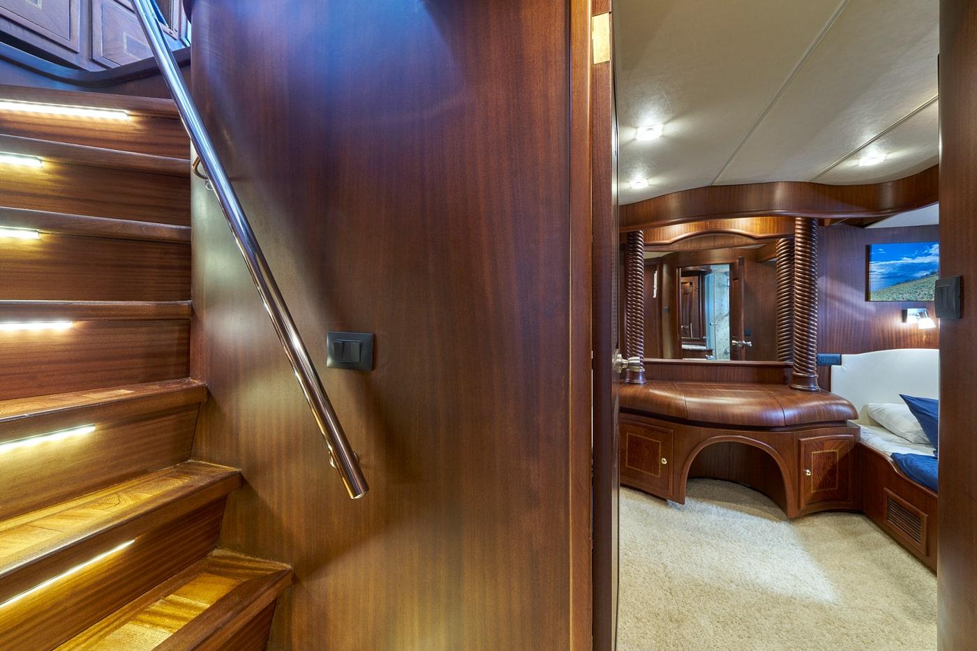 yacht interior showing wooden staircase with handrail and cabin entrance with vanity area