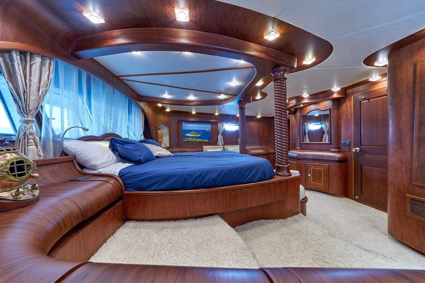 luxury yacht master cabin featuring curved wooden canopy bed with blue bedding and multiple portholes