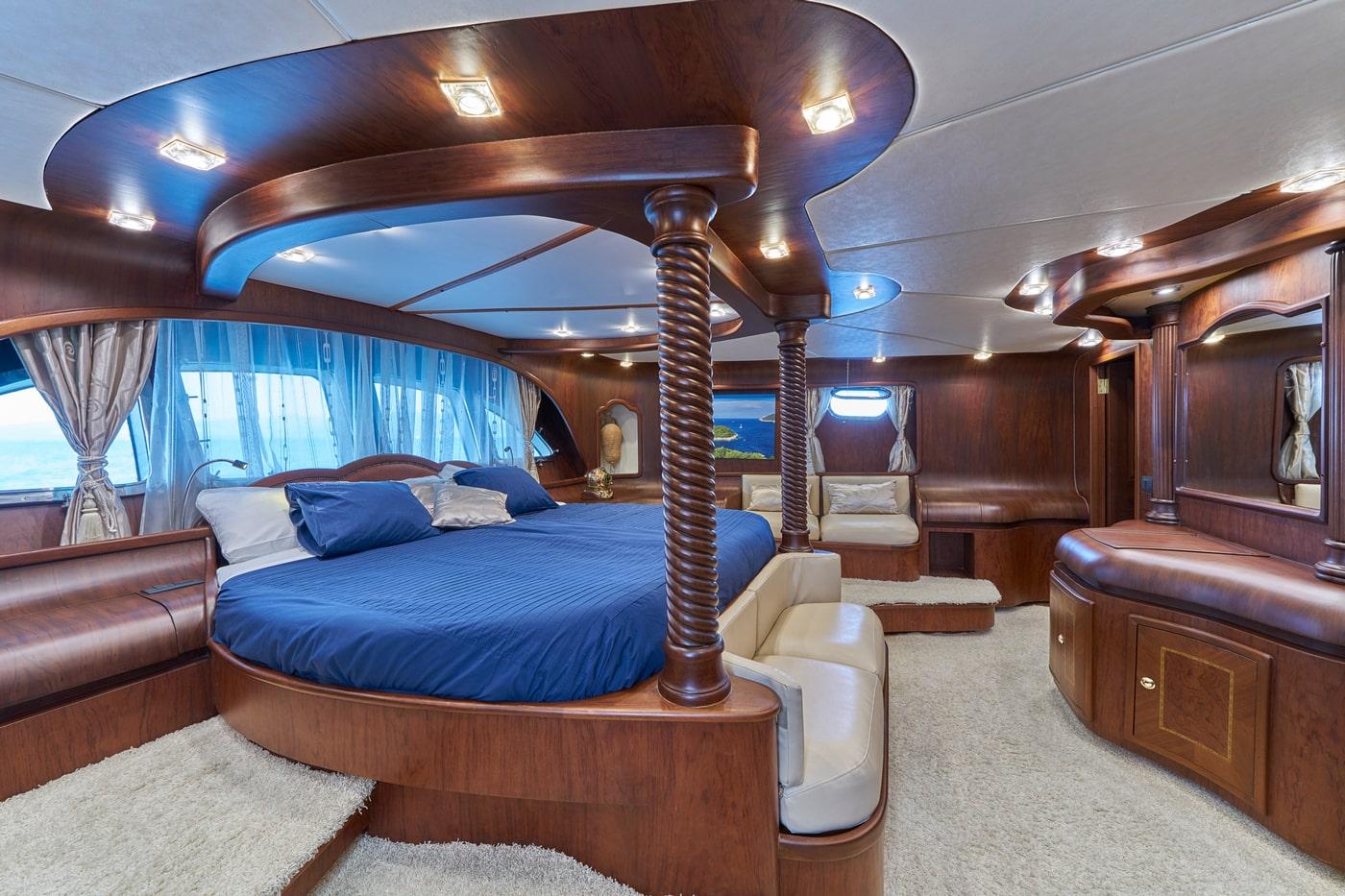 Master cabin featuring round bed with blue bedding, twisted wooden posts, cream leather seating and panoramic windows