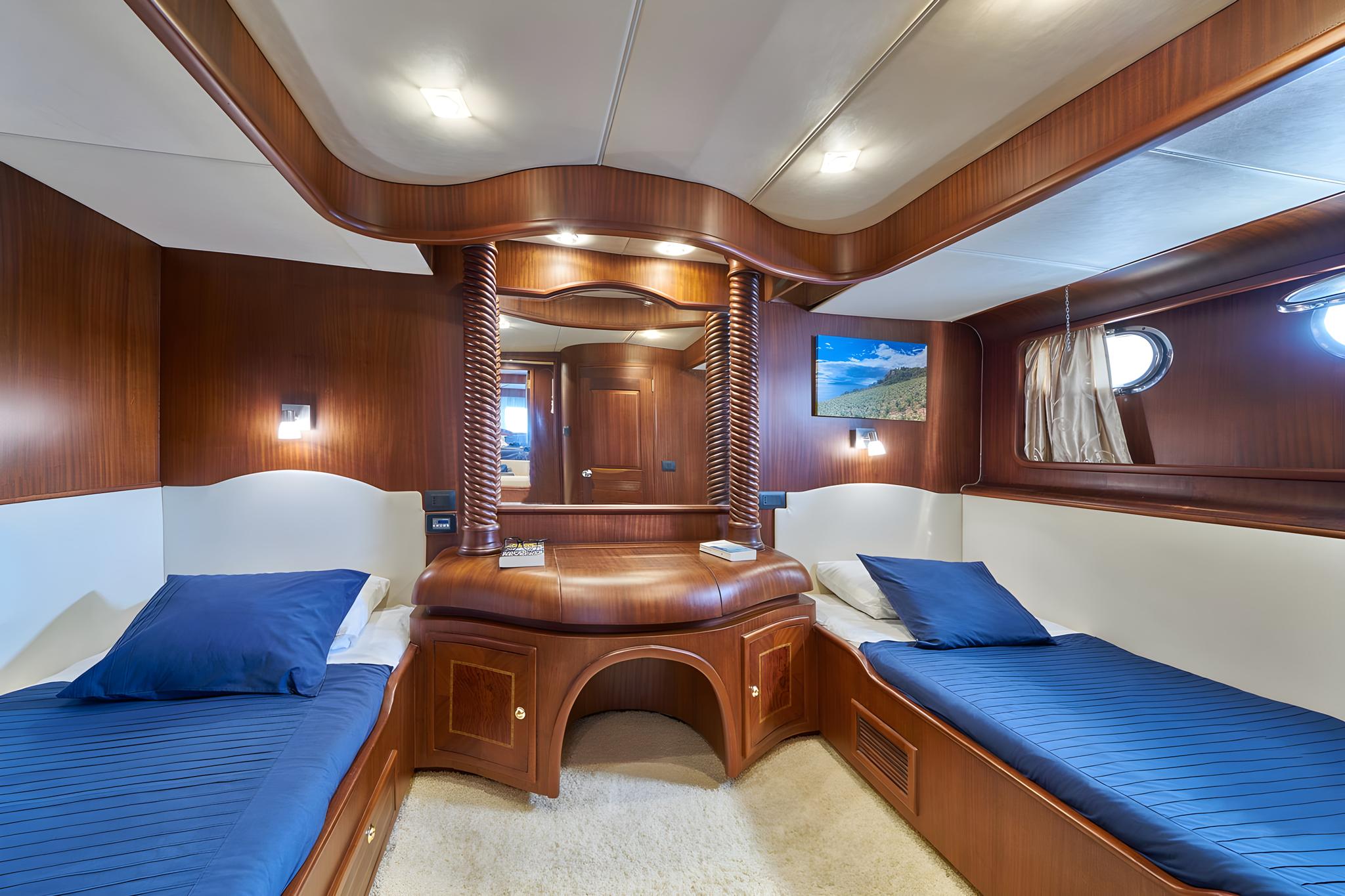 yacht guest cabin featuring twin beds with blue bedding and decorative carved wooden posts