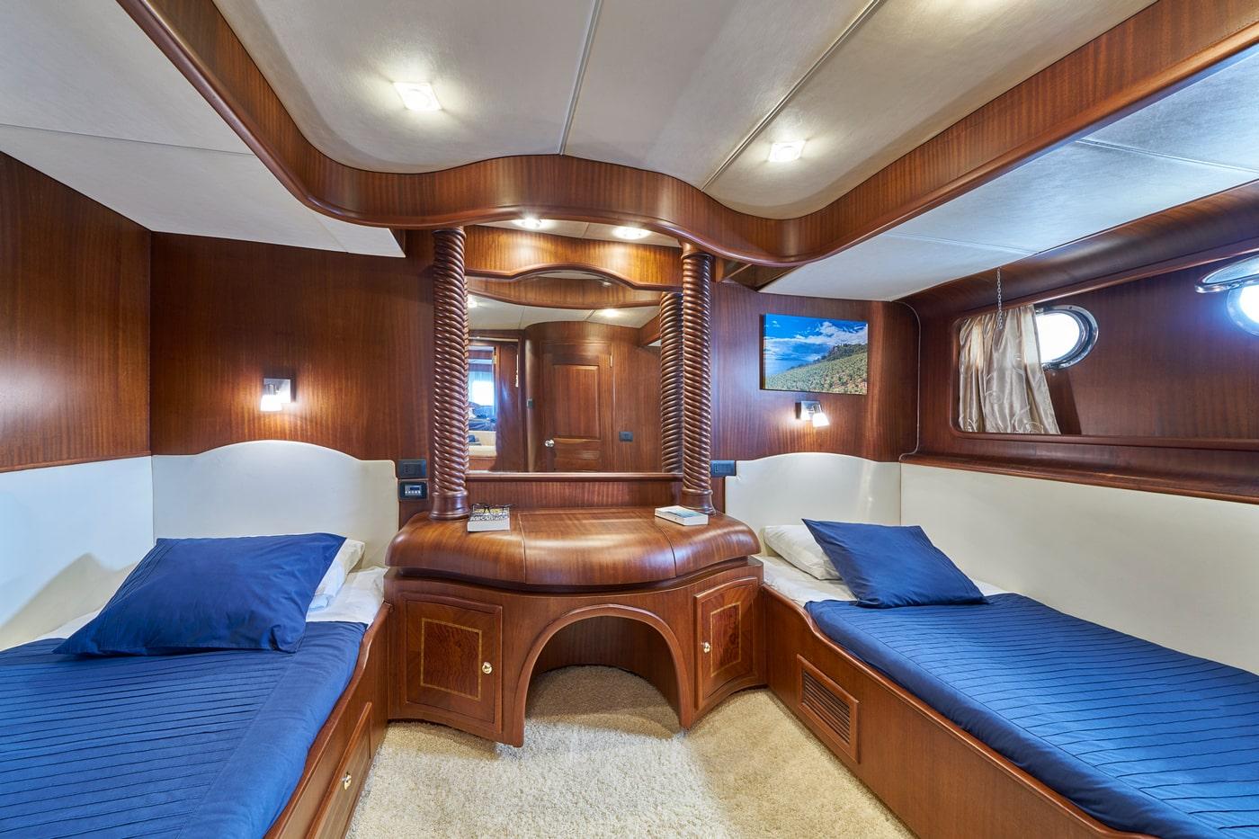 yacht guest cabin featuring twin beds with blue bedding and decorative carved wooden posts