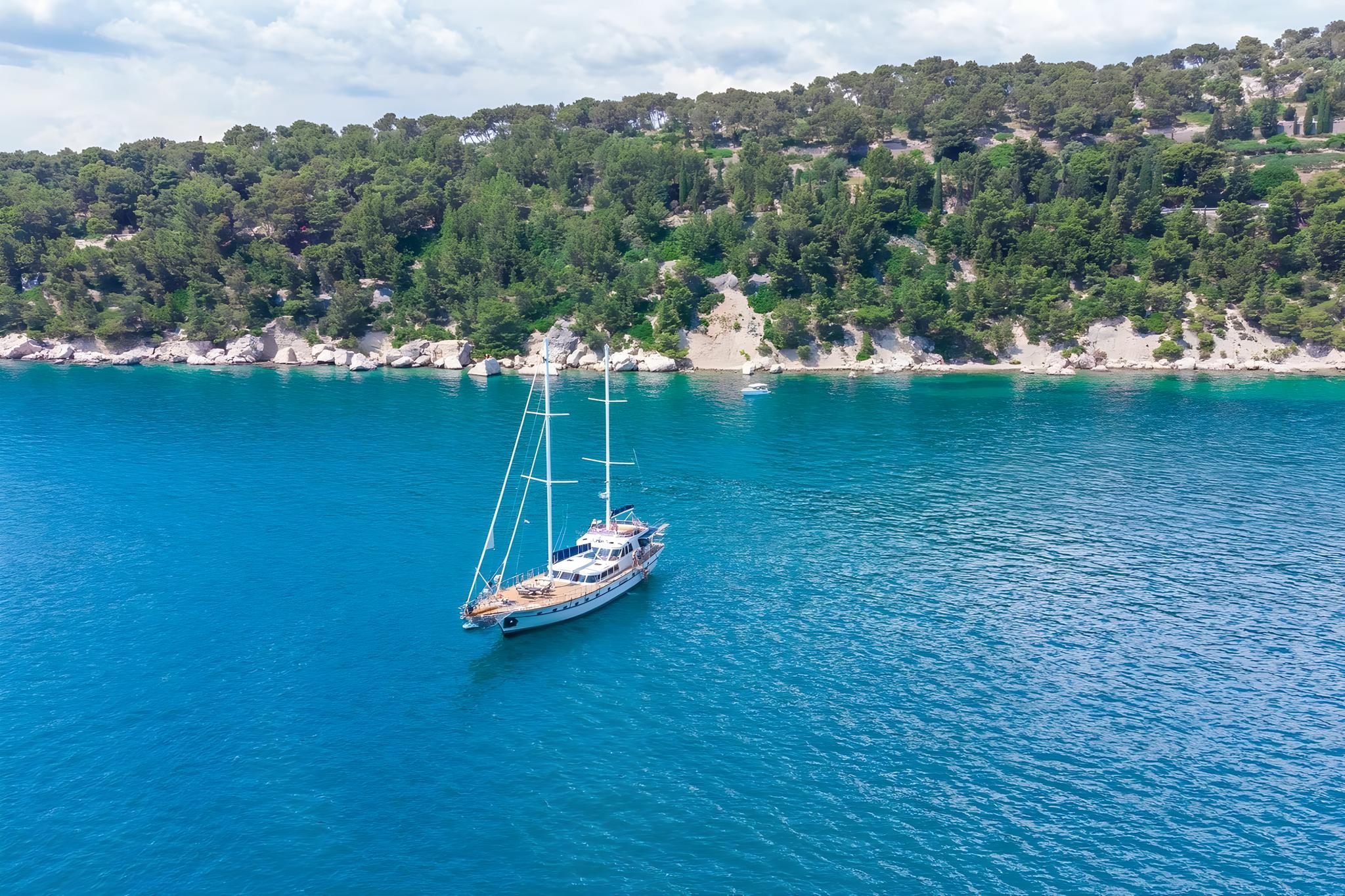 aerial view of traditional gulet yacht anchored in pristine turquoise bay near forested coastline