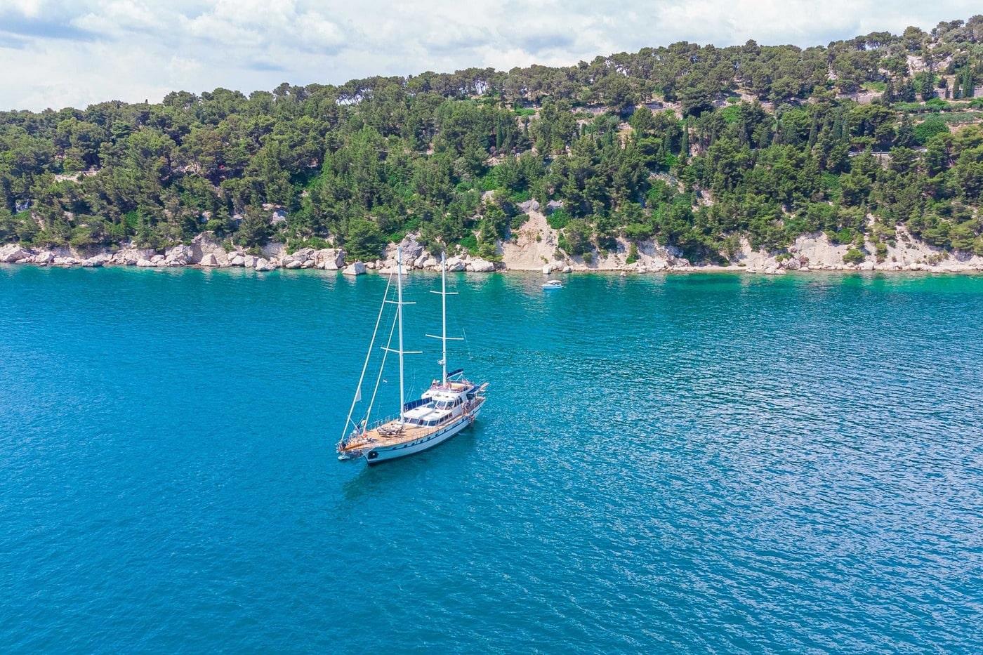 aerial view of traditional gulet yacht anchored in pristine turquoise bay near forested coastline