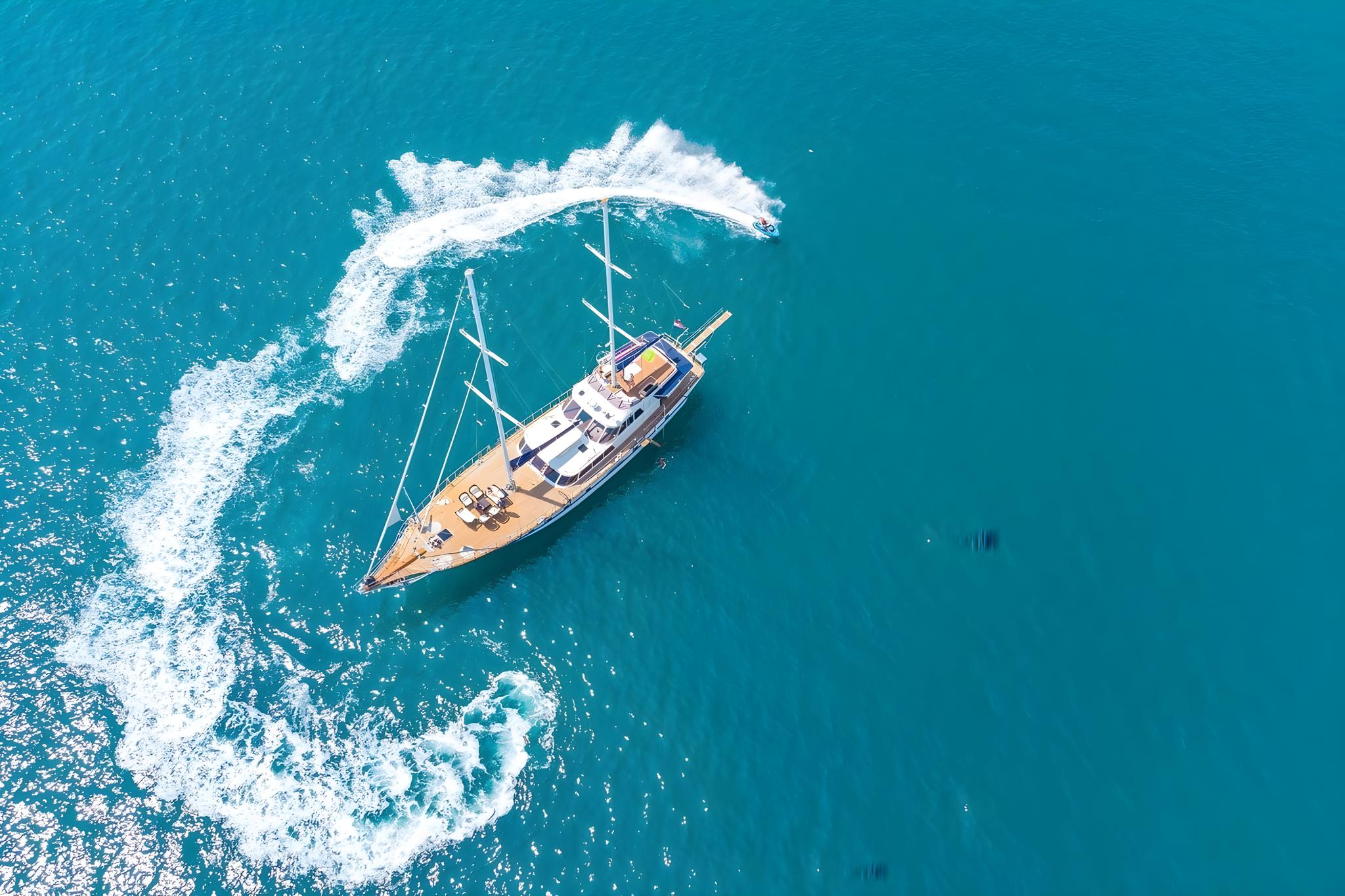 aerial view of traditional gulet yacht anchored in turquoise waters with distinctive white wake pattern