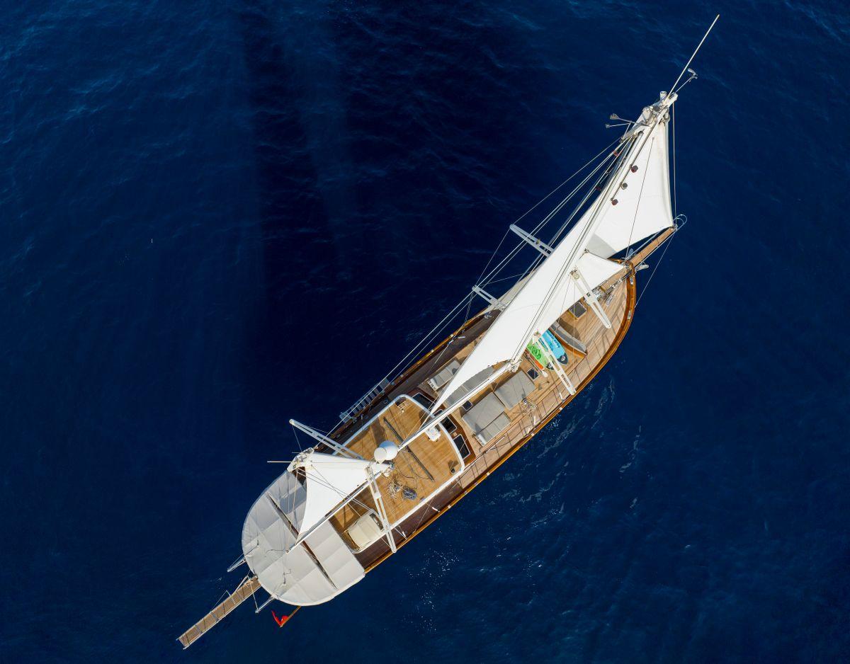 aerial view of traditional wooden gulet yacht with white sails and teak decks on deep blue Mediterranean waters