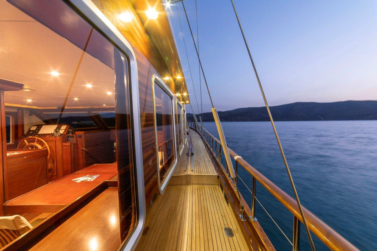 yacht side deck walkway with teak flooring, steel railings and illuminated helm area at dusk