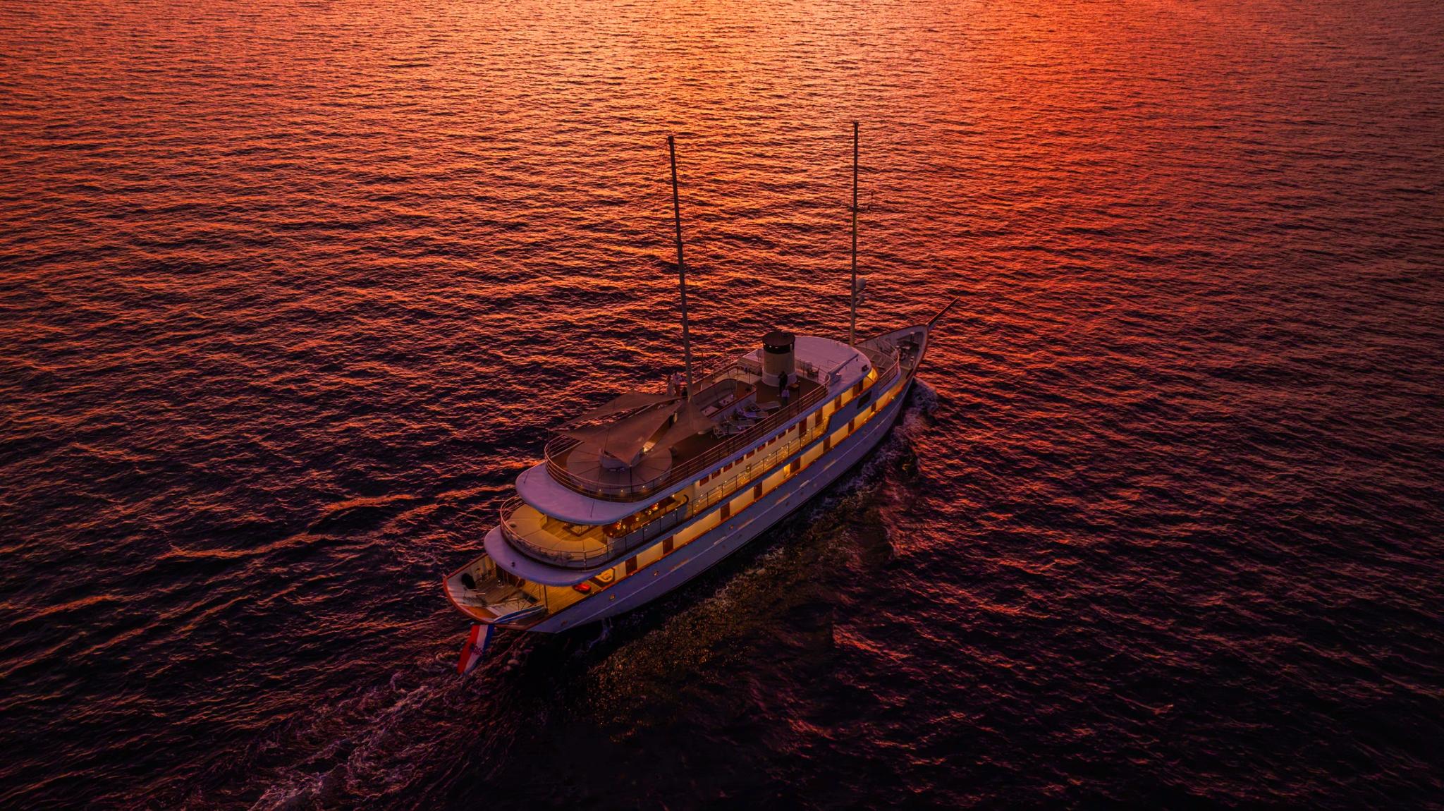 aerial view of illuminated luxury yacht at sunset on calm orange-tinted waters