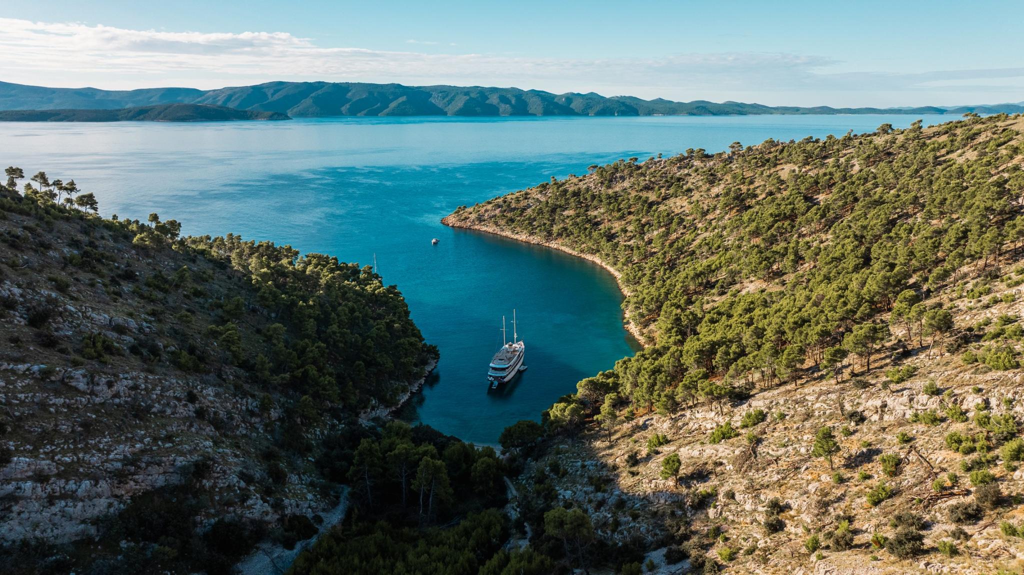 aerial view of luxury gulet yacht anchored in protected turquoise bay surrounded by forested hills