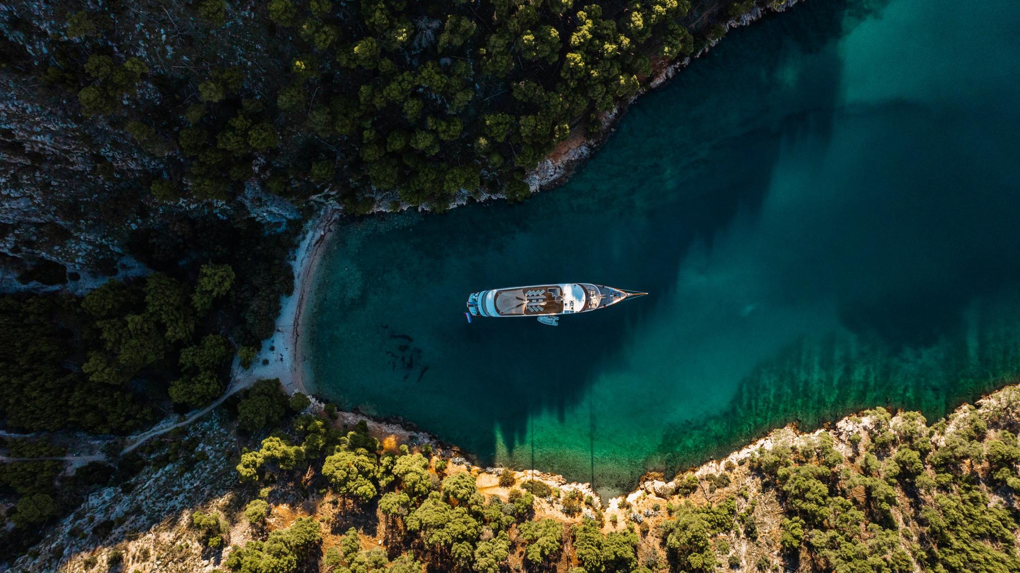 aerial view of luxury gulet yacht anchored in secluded turquoise bay surrounded by forested coastline