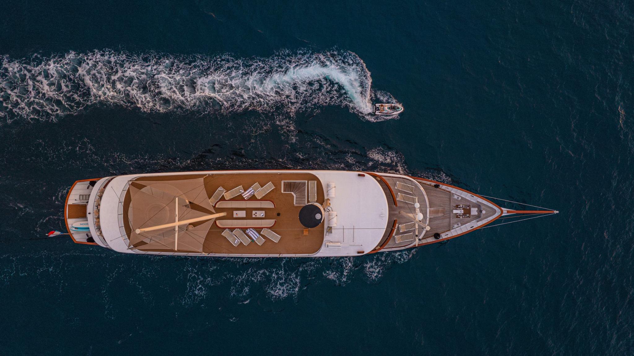 aerial drone shot of luxury yacht with teak decks and tender creating wake in blue water