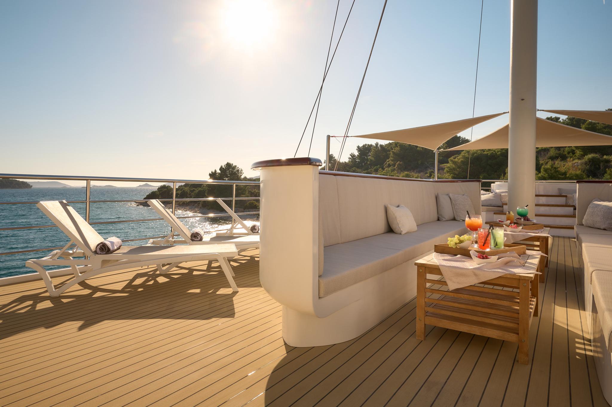 yacht aft deck with built-in seating, coffee table, sun loungers and sea views