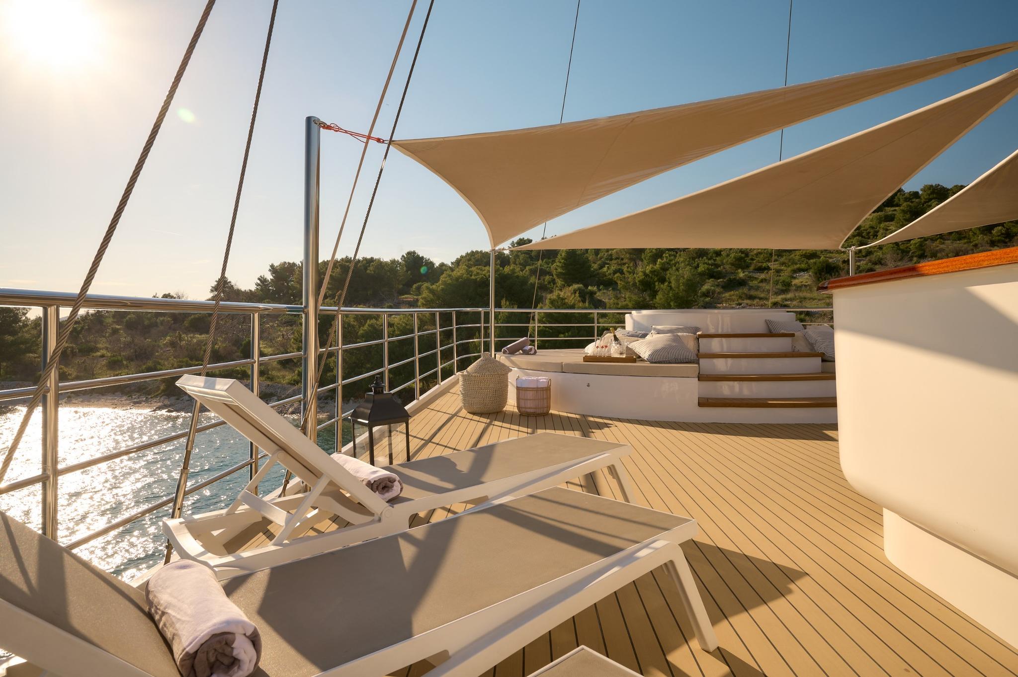 yacht bow sun deck with white loungers, beige shade sails and teak decking