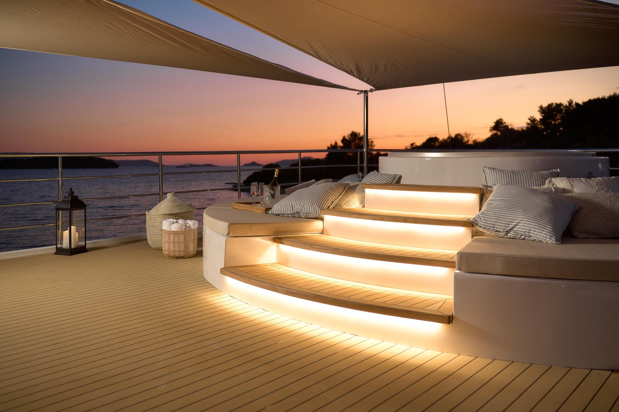 yacht upper deck seating area with LED-lit steps and cushions at sunset