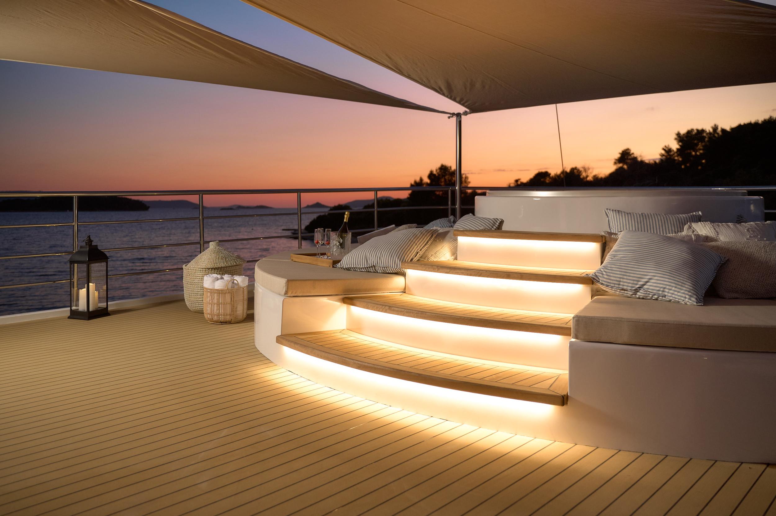 yacht upper deck seating area with LED-lit steps and cushions at sunset