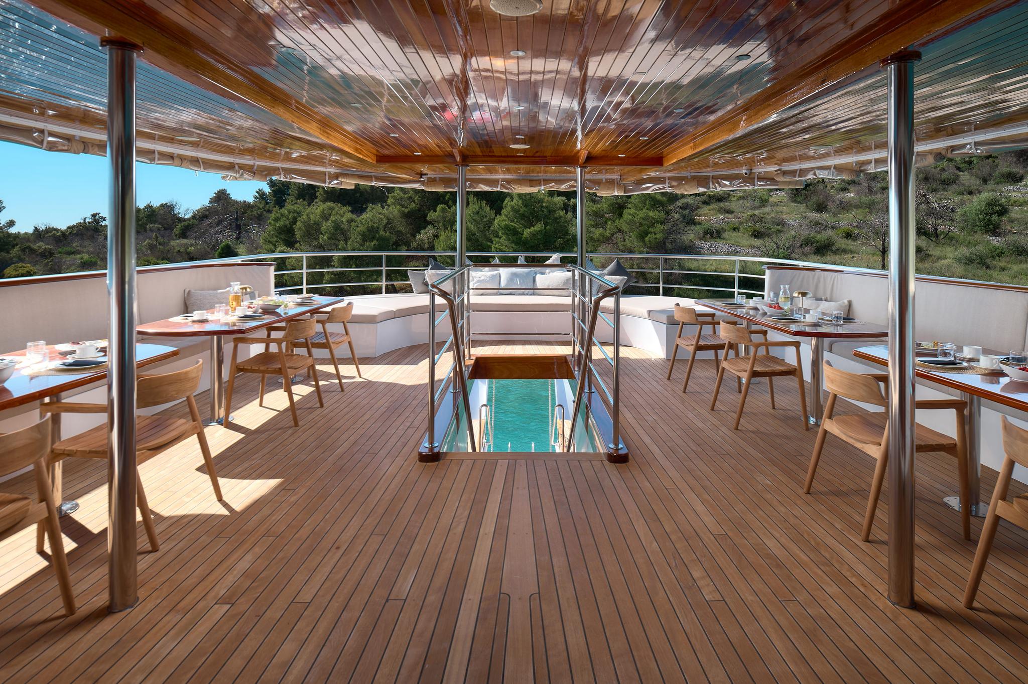yacht aft deck dining area with teak flooring, glass floor panel, and coastal views