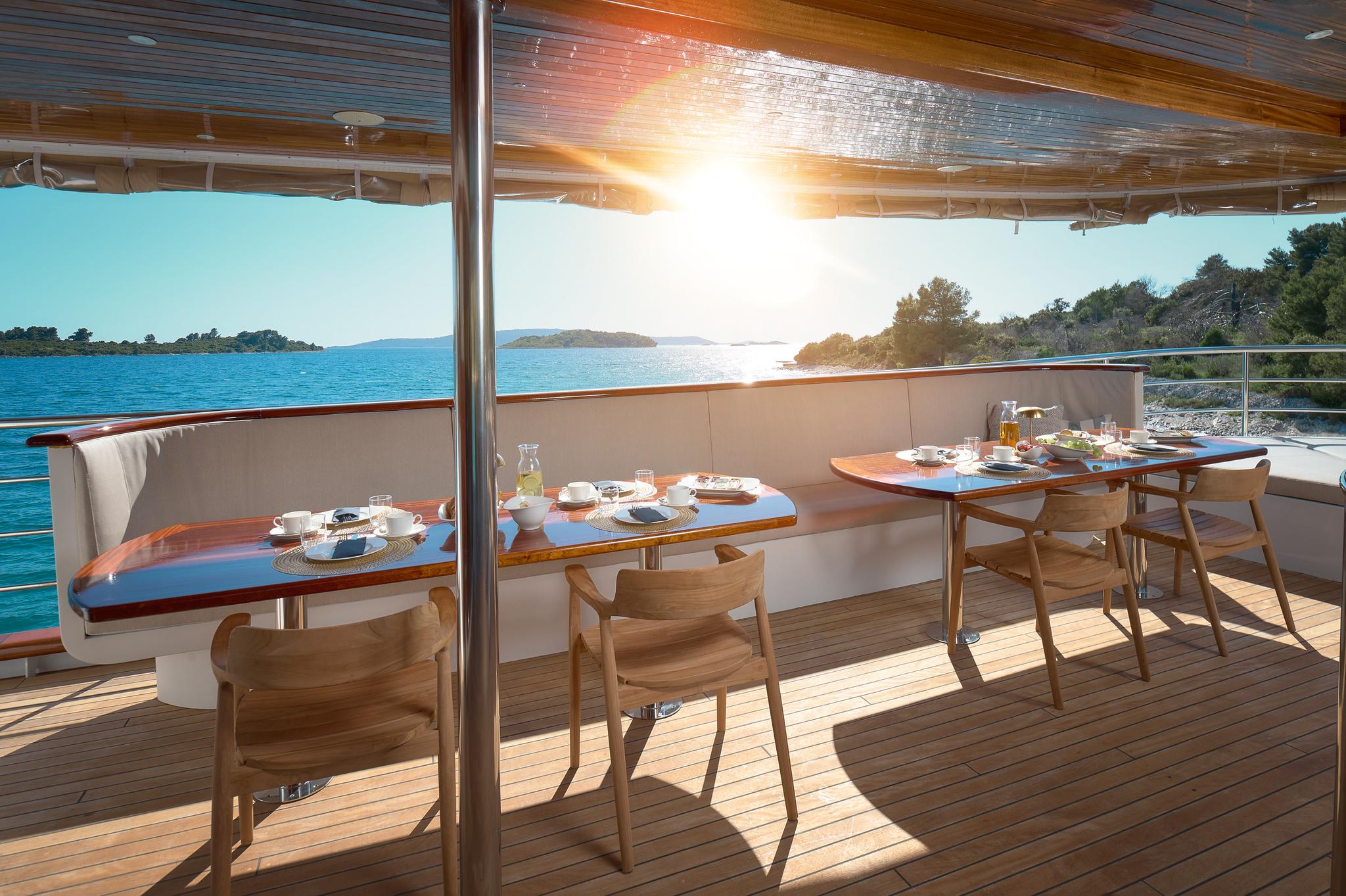 yacht aft deck dining area with breakfast table settings and coastal sunrise view
