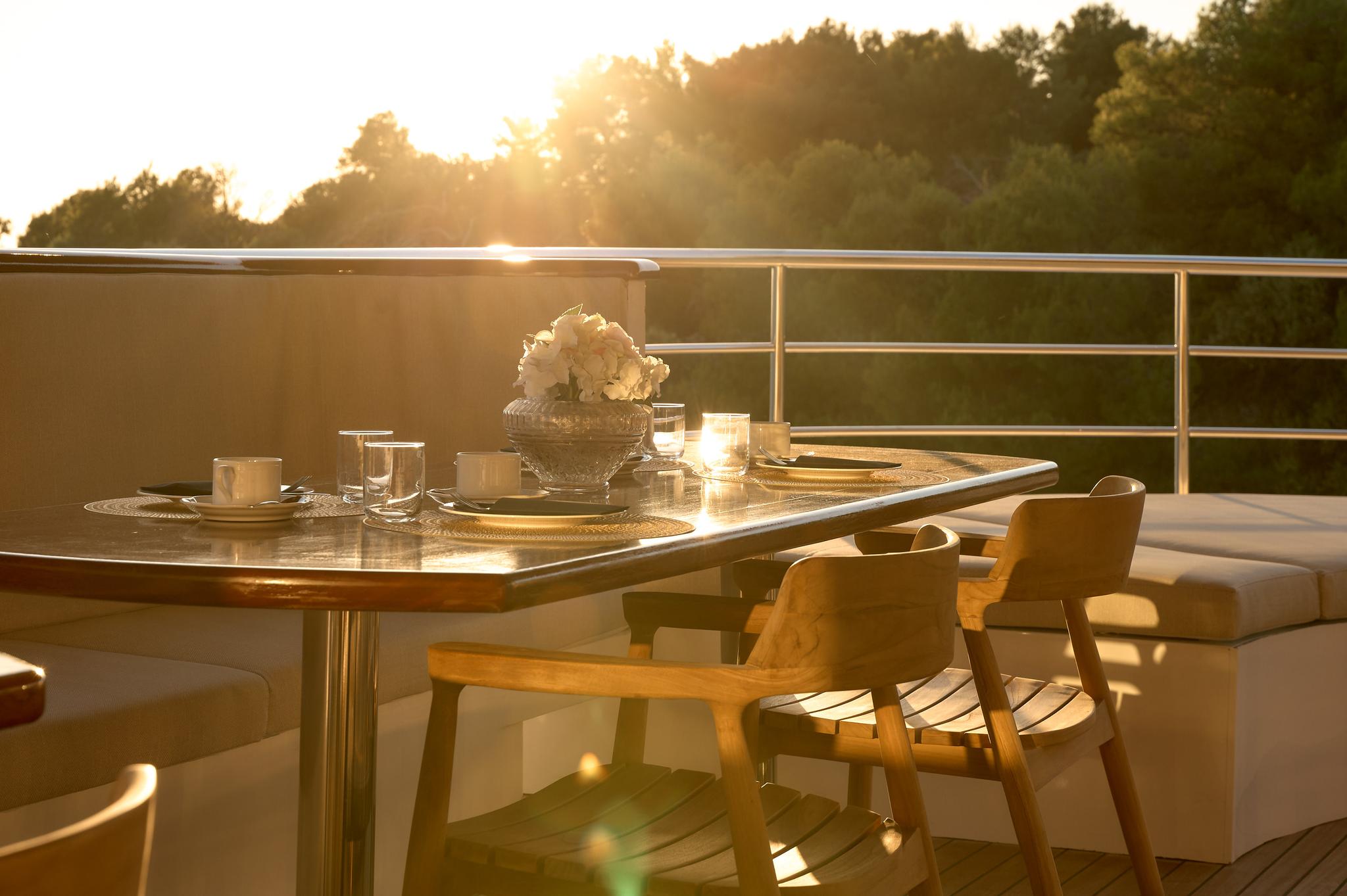 yacht deck dining table with place settings and flower centerpiece at golden hour