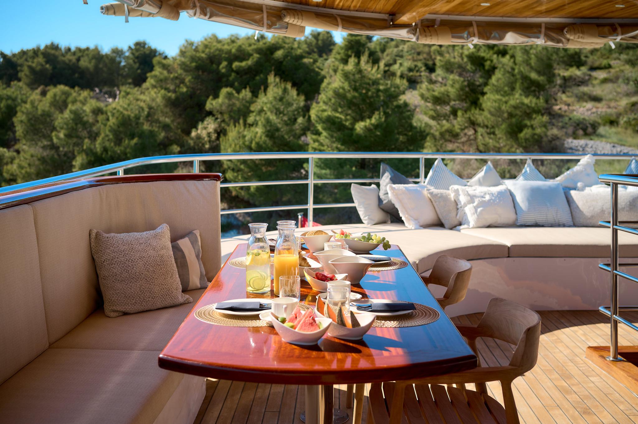 yacht aft deck dining table set with breakfast plates, fresh fruit, and orange juice