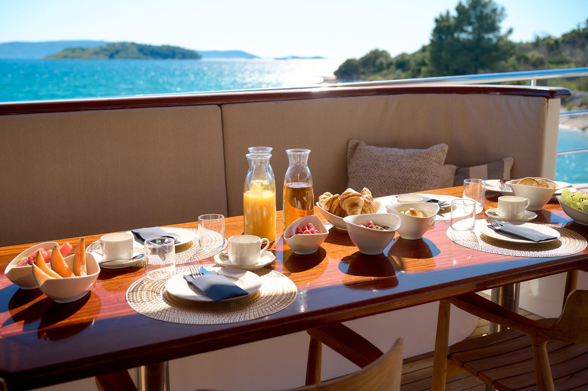 yacht breakfast table with croissants, fresh fruit, orange juice and coffee served on deck
