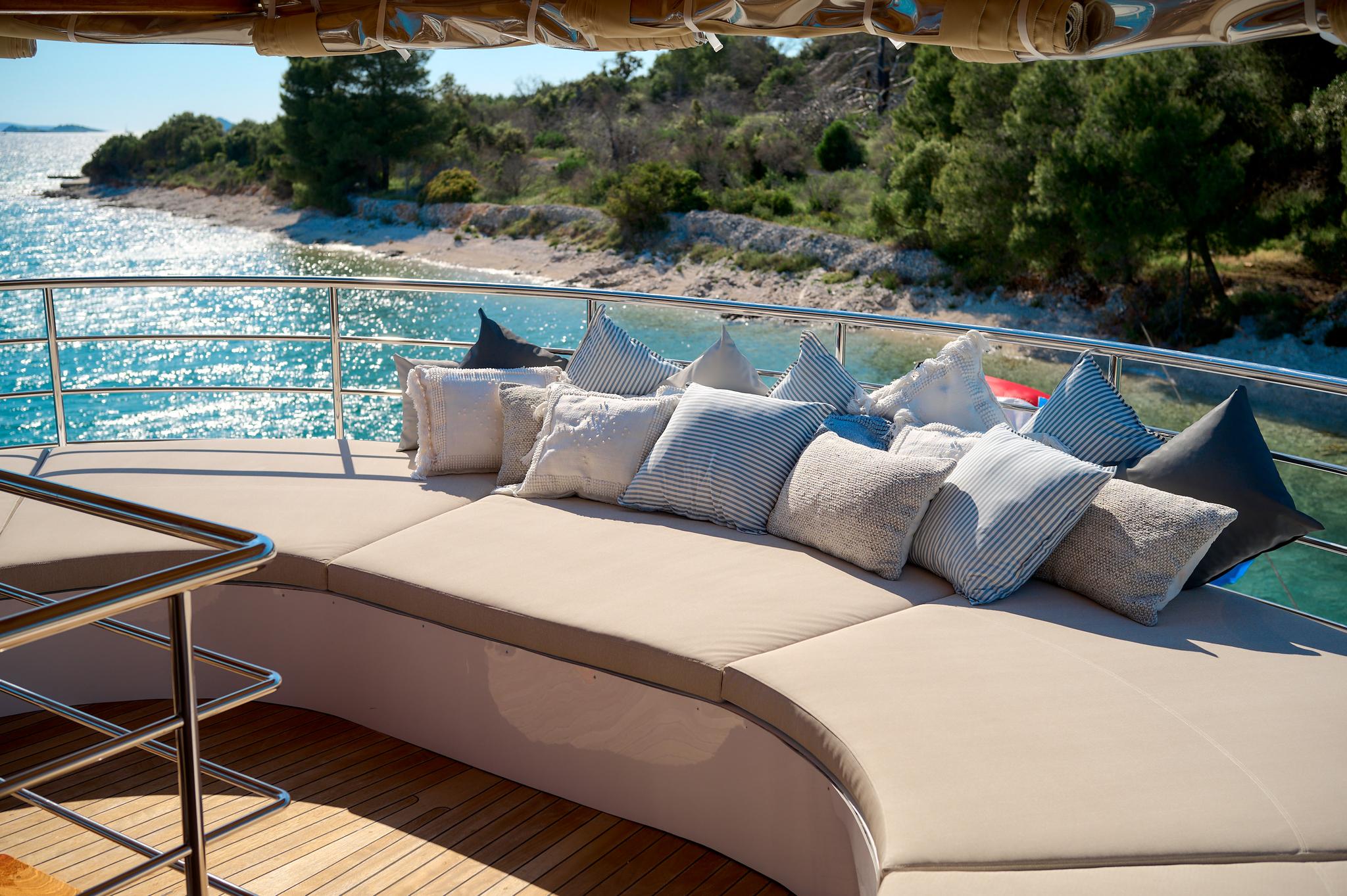 curved outdoor lounge seating with striped and neutral cushions on yacht aft deck overlooking coastline