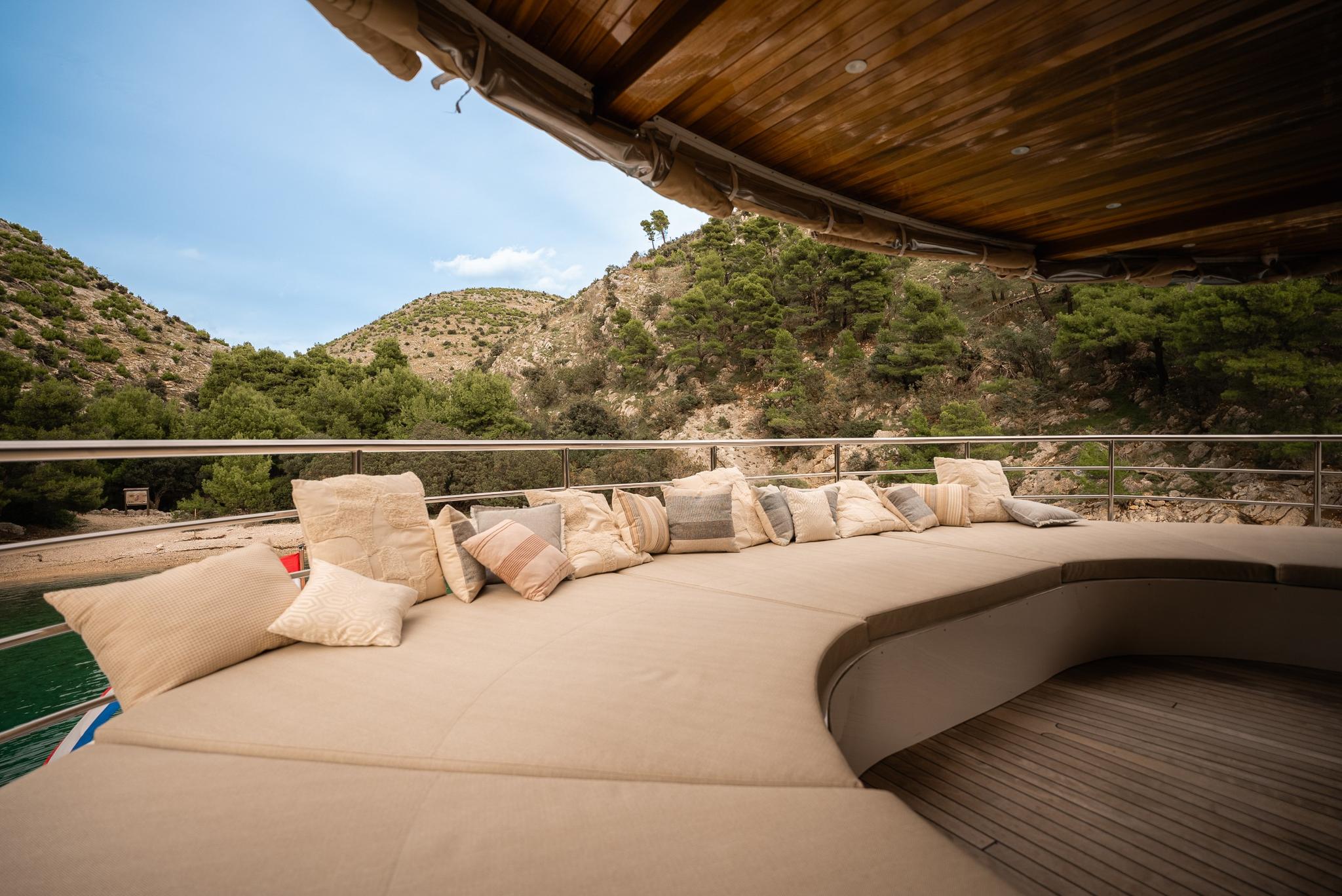 curved outdoor lounge seating with beige cushions on yacht deck overlooking mountainous coastline