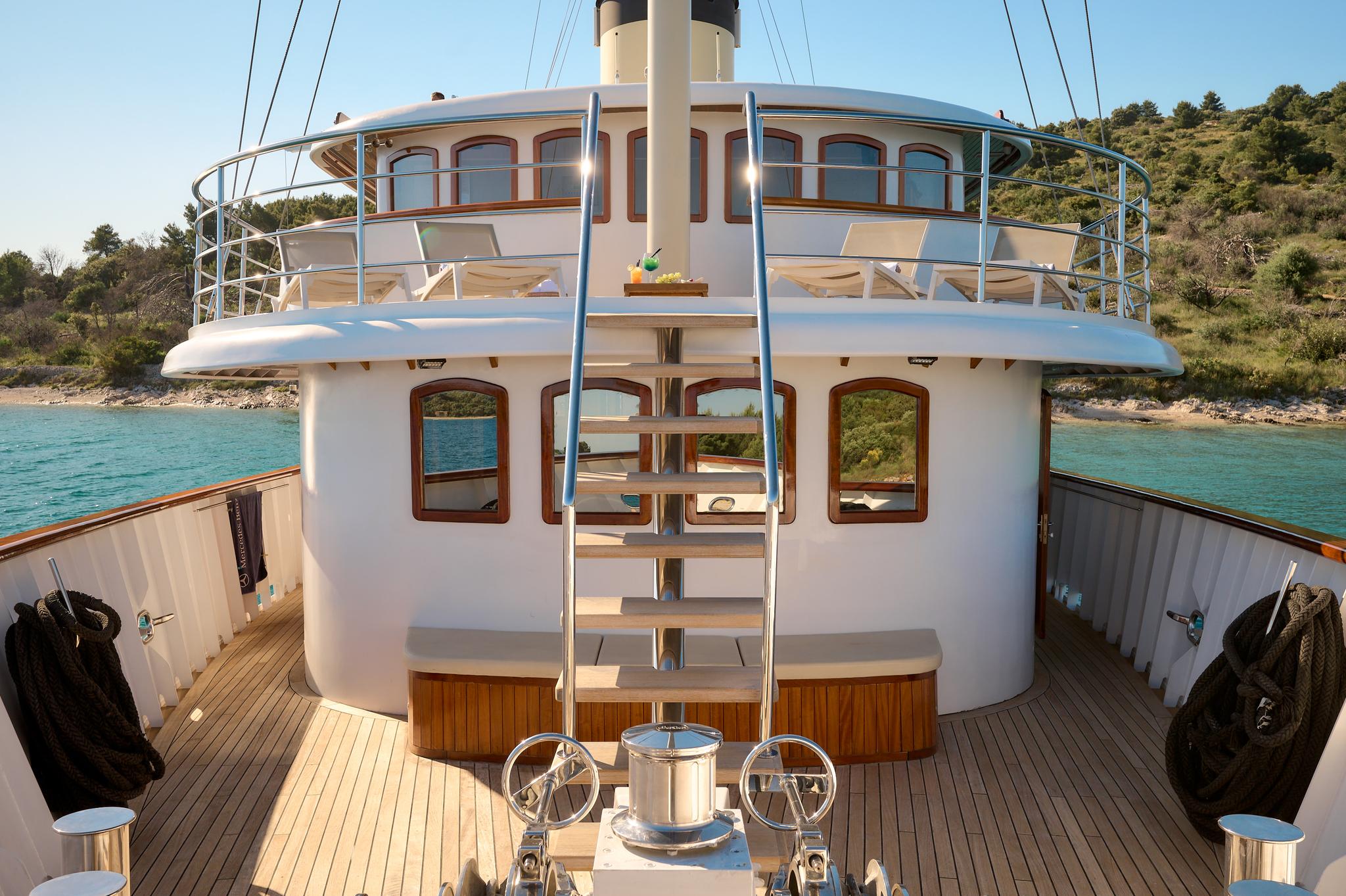 gulet stern deck with teak decking, central wheelhouse structure, stainless steel ladder and twin helm stations
